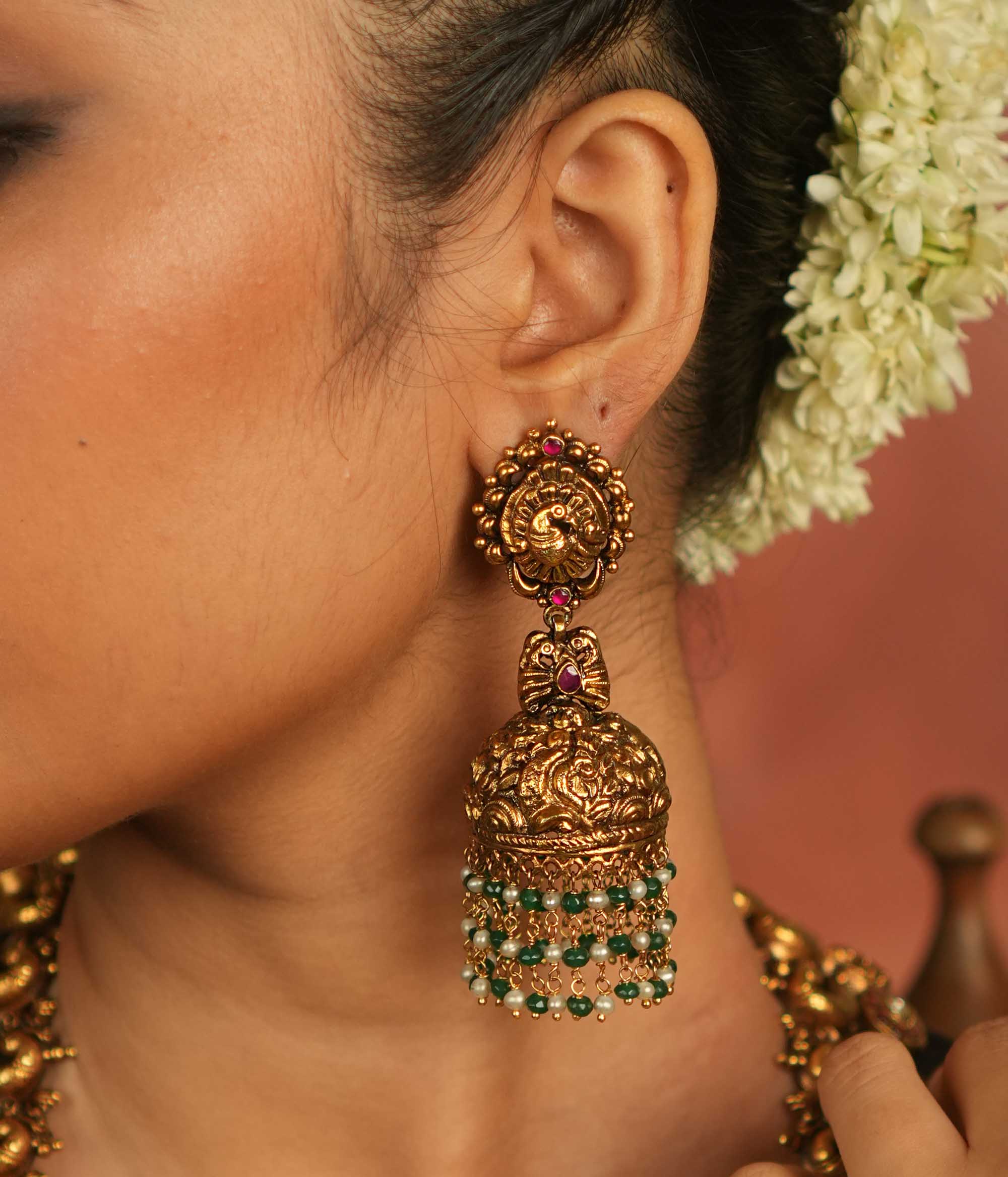Mystic echoes reborn! Antique gold-plated jhumka adorned with red kundan, green and white bead droplets, exudes a peacock’s graceful opulence—an eternal treasure.
