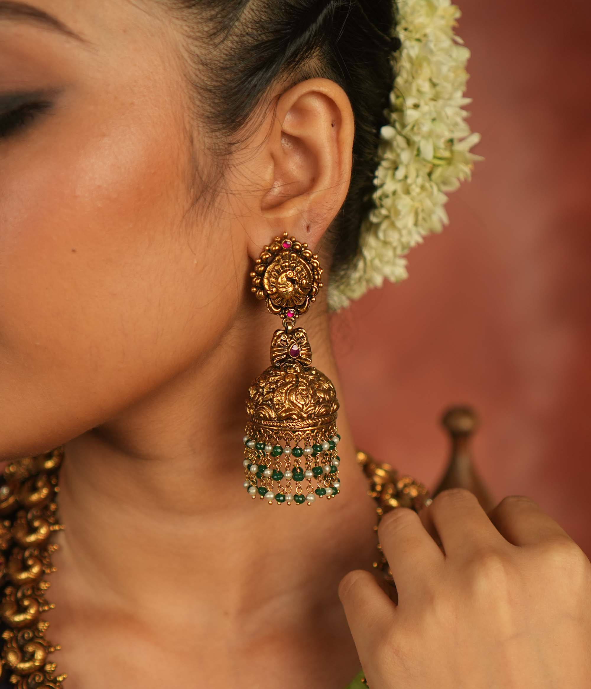 Mystic echoes reborn! Antique gold-plated jhumka adorned with red kundan, green and white bead droplets, exudes a peacock’s graceful opulence—an eternal treasure.