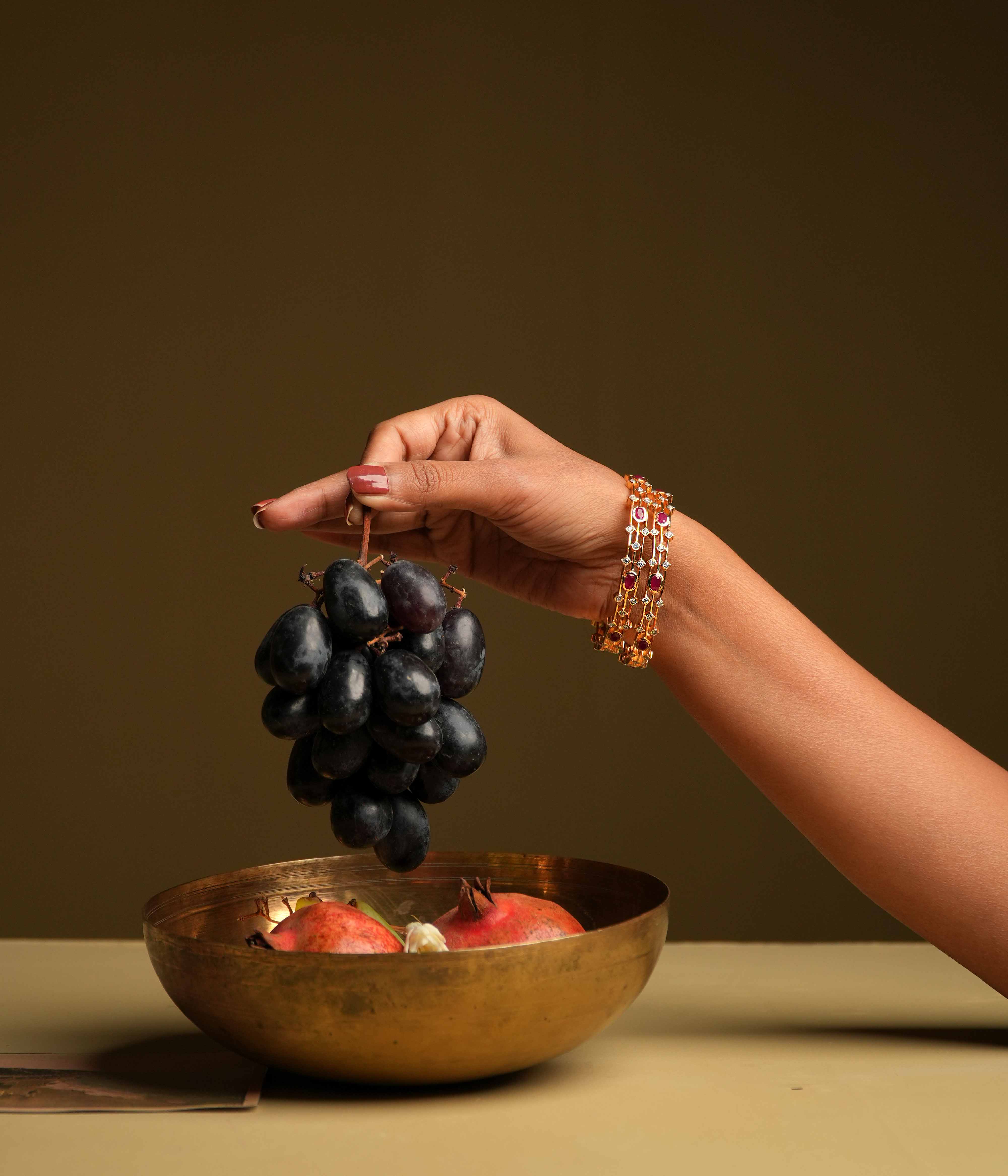 A triple-lined 92.5 sterling silver bangle with an insert type closure, showcasing clusters of moissanite and red oval gemstones intricately set with traditional diamond setting techniques, blending majestic elegance with modern sophistication.