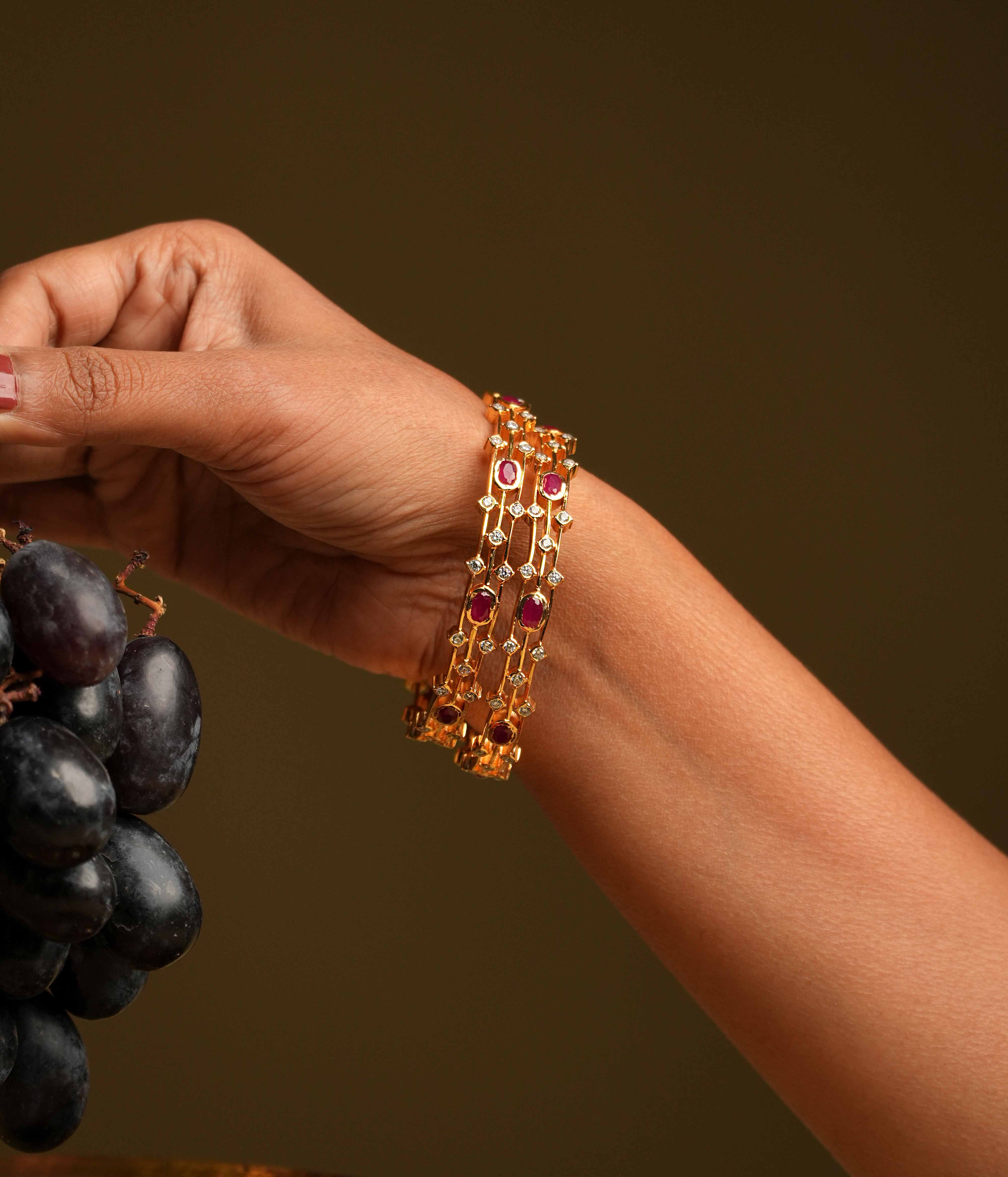 A triple-lined 92.5 sterling silver bangle with an insert type closure, showcasing clusters of moissanite and red oval gemstones intricately set with traditional diamond setting techniques, blending majestic elegance with modern sophistication.
