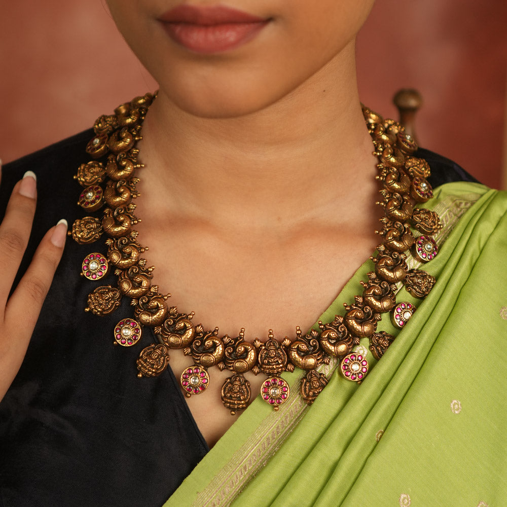 Regal whispers reborn in an antique gold-plated necklace, where floral and goddess motifs adorned with red and white kundan stones radiate timeless royal grace.