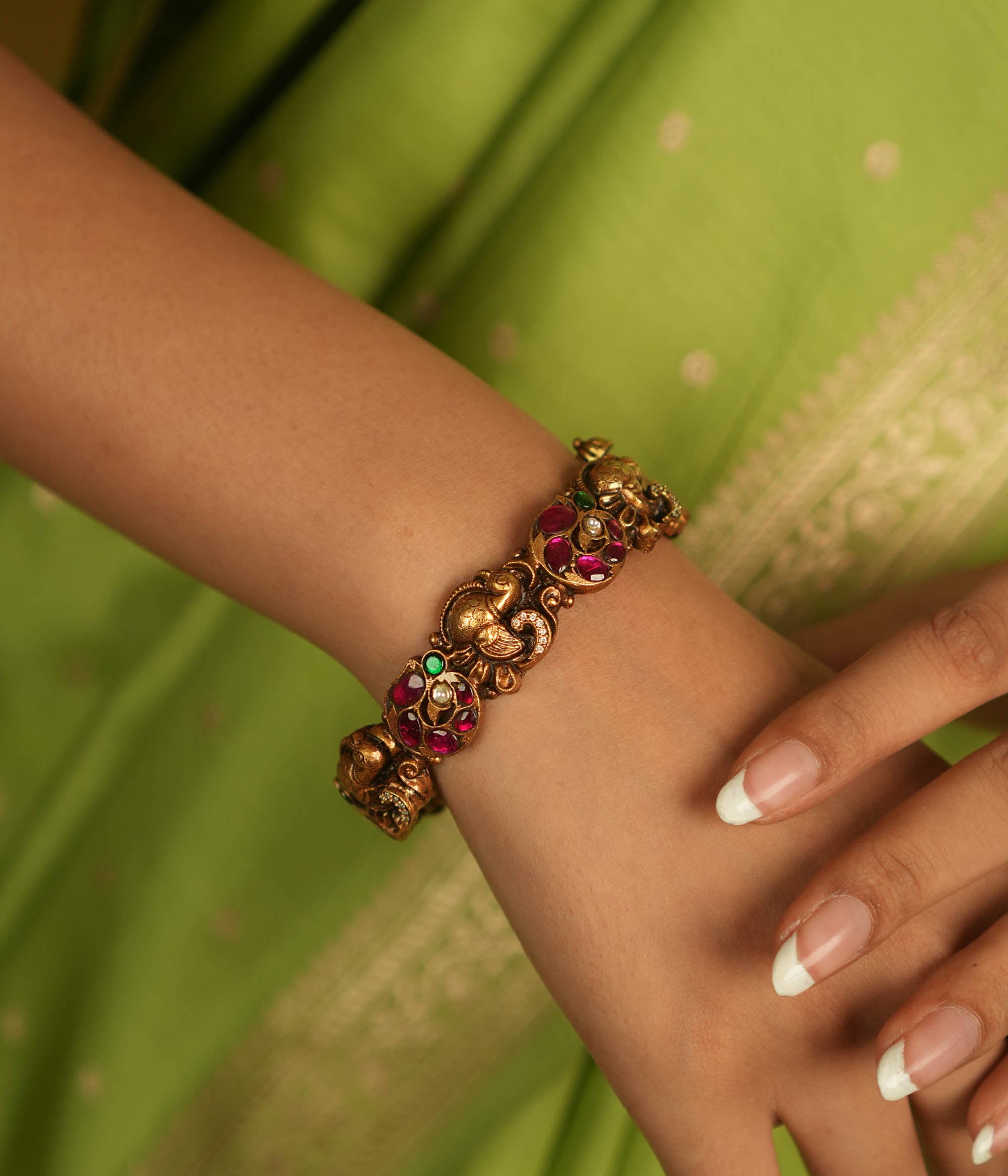 Regal whispers reborn in an antique gold-plated bangle, where peacock motifs and vibrant kundan stones echo timeless heritage and artistry.