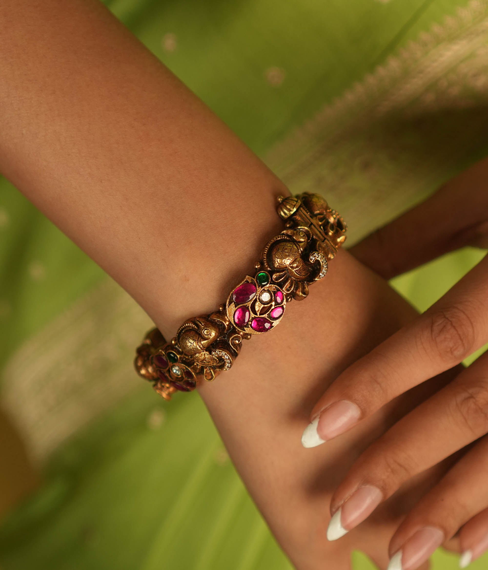 Regal whispers reborn in an antique gold-plated bangle, where peacock motifs and vibrant kundan stones echo timeless heritage and artistry.