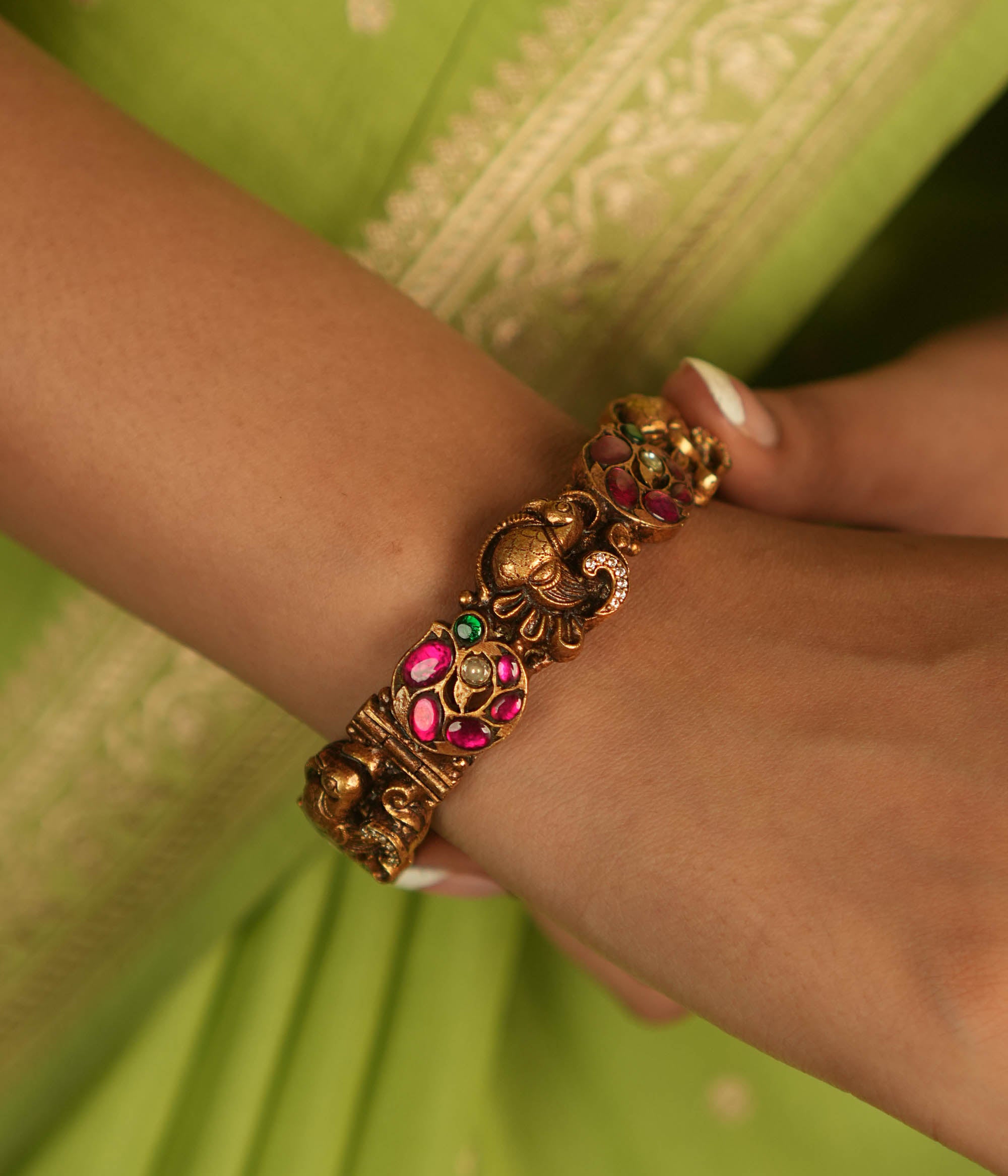 Regal whispers reborn in an antique gold-plated bangle, where peacock motifs and vibrant kundan stones echo timeless heritage and artistry.