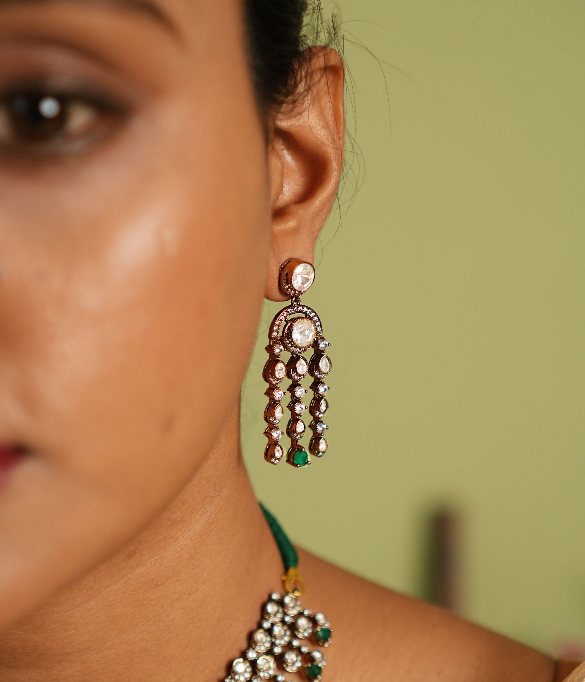 Echoes of a bygone era reborn! These gold-plated silver dangler earrings feature floral-shaped droplets adorned with Polki, CZ stones, and green spinal gems, cascading like delicate vines. A timeless blend of Victorian charm and graceful allure.