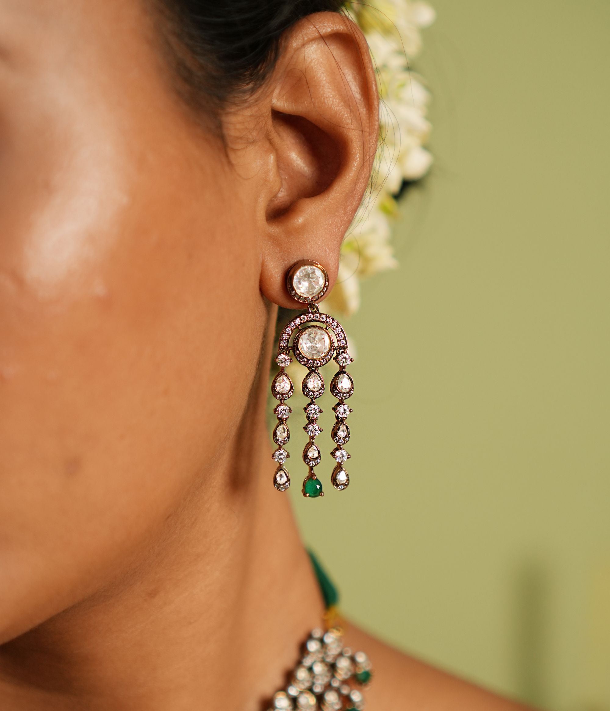 Echoes of a bygone era reborn! These gold-plated silver dangler earrings feature floral-shaped droplets adorned with Polki, CZ stones, and green spinal gems, cascading like delicate vines. A timeless blend of Victorian charm and graceful allure.