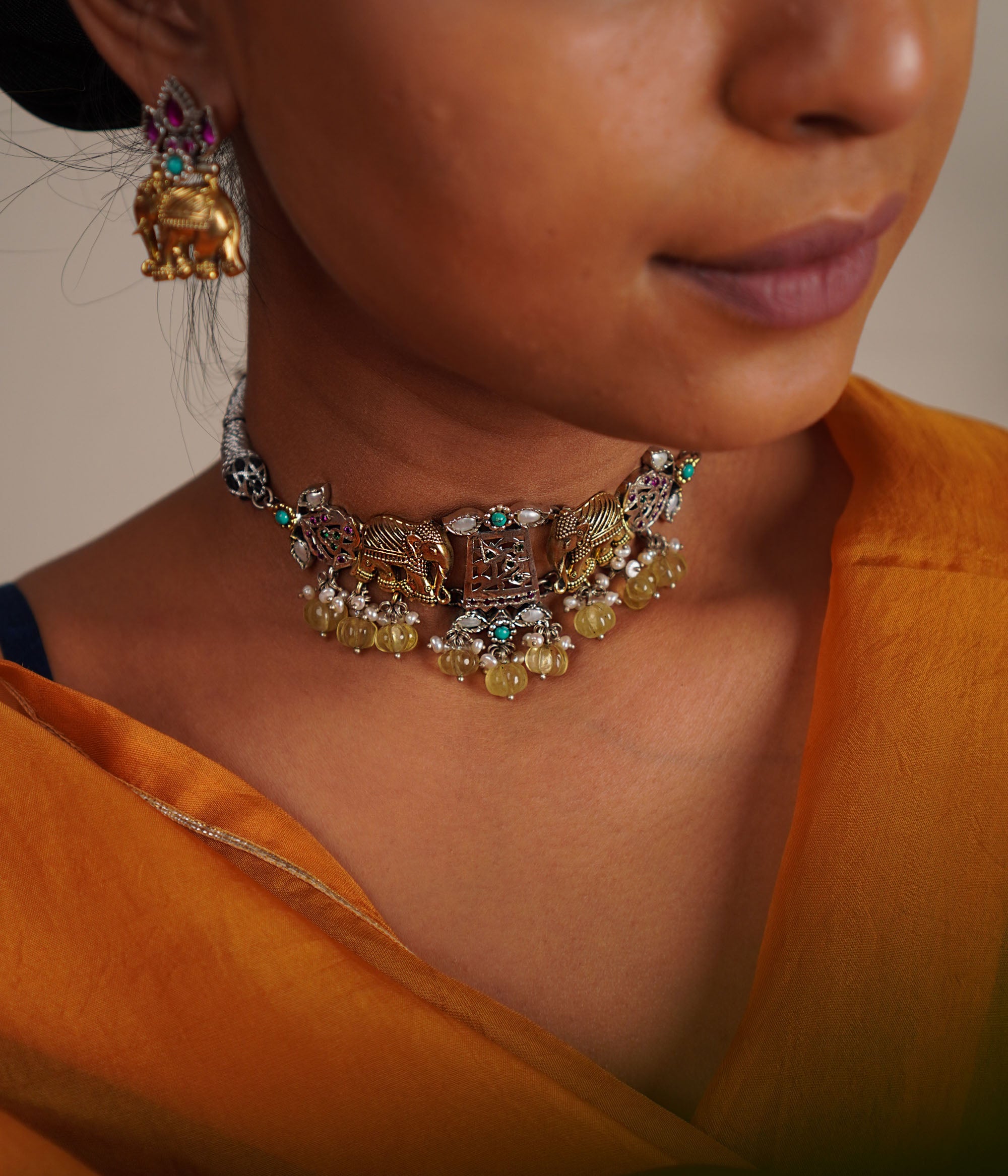 This oxidized silver choker, adorned with white, red, and green kundan stones and delicate pearl droplets, features regal gold-plated elephant motifs at its heart. A timeless piece that evokes the grandeur of a bygone era, reminiscent of a treasured heirloom.