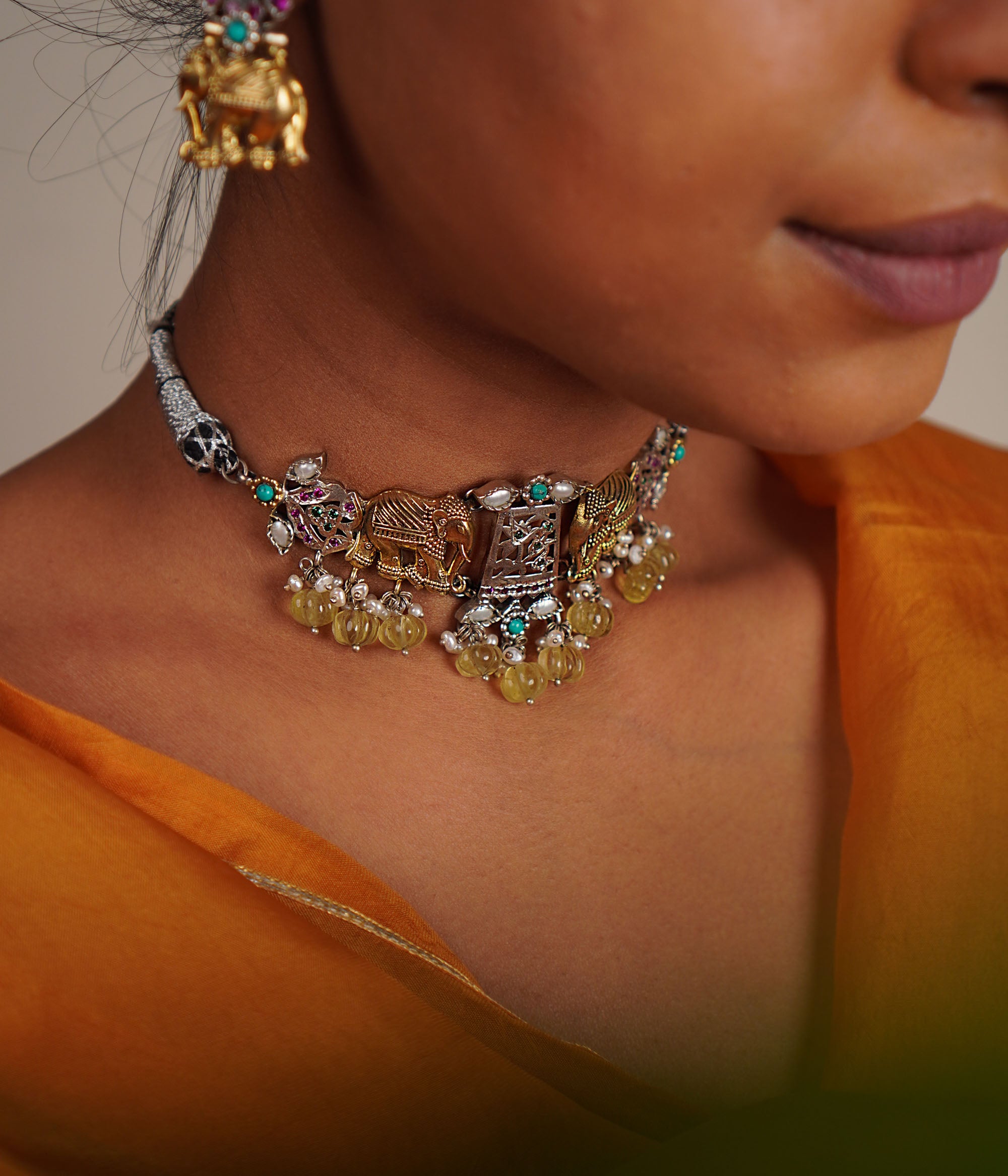 This oxidized silver choker, adorned with white, red, and green kundan stones and delicate pearl droplets, features regal gold-plated elephant motifs at its heart. A timeless piece that evokes the grandeur of a bygone era, reminiscent of a treasured heirloom.