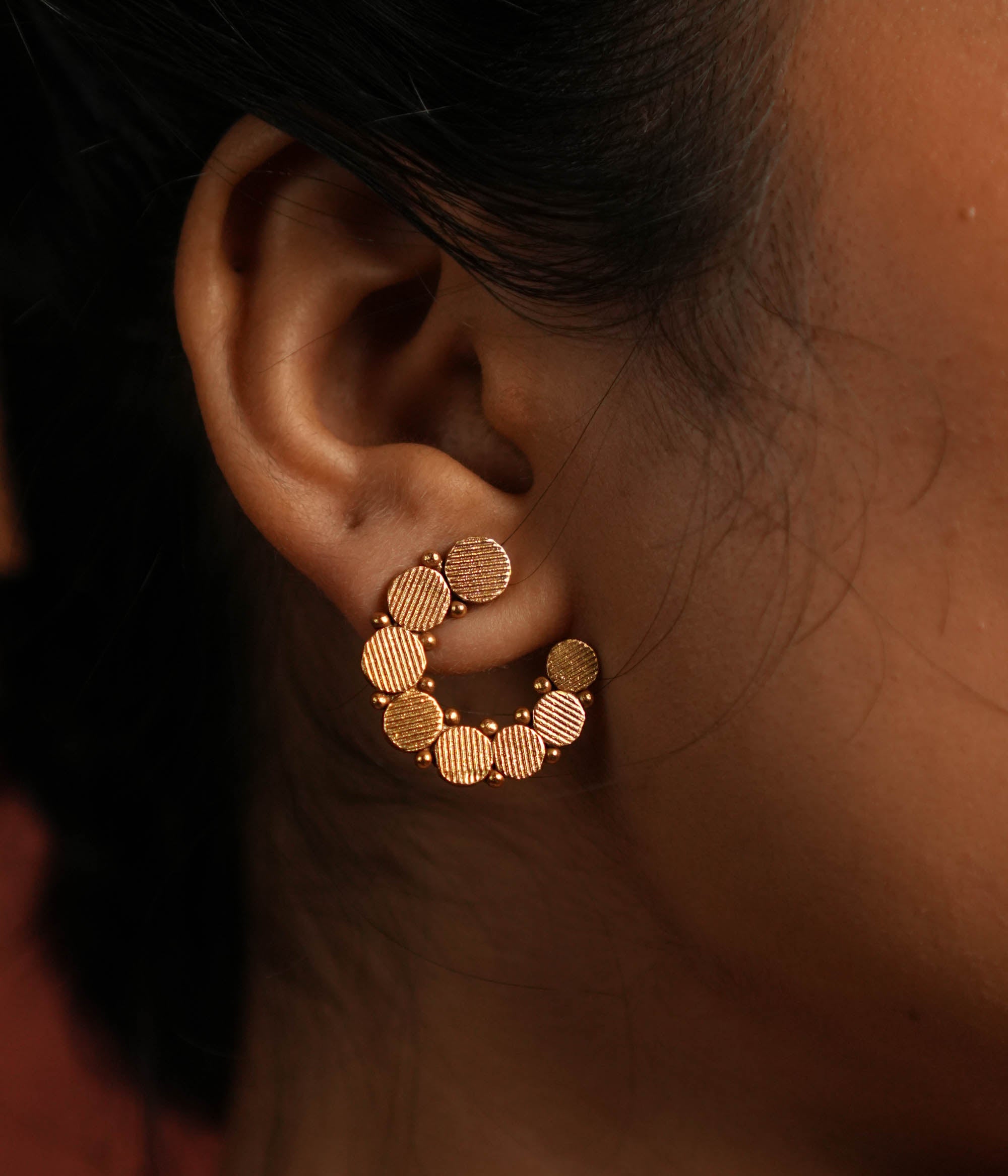 These gold-plated silver stud earrings showcase dainty coin-like motifs arranged in a graceful circular pattern. Inspired by vintage Kolhapuri tribal designs, they blend tradition with elegance, making them a timeless addition to any jewelry collection.