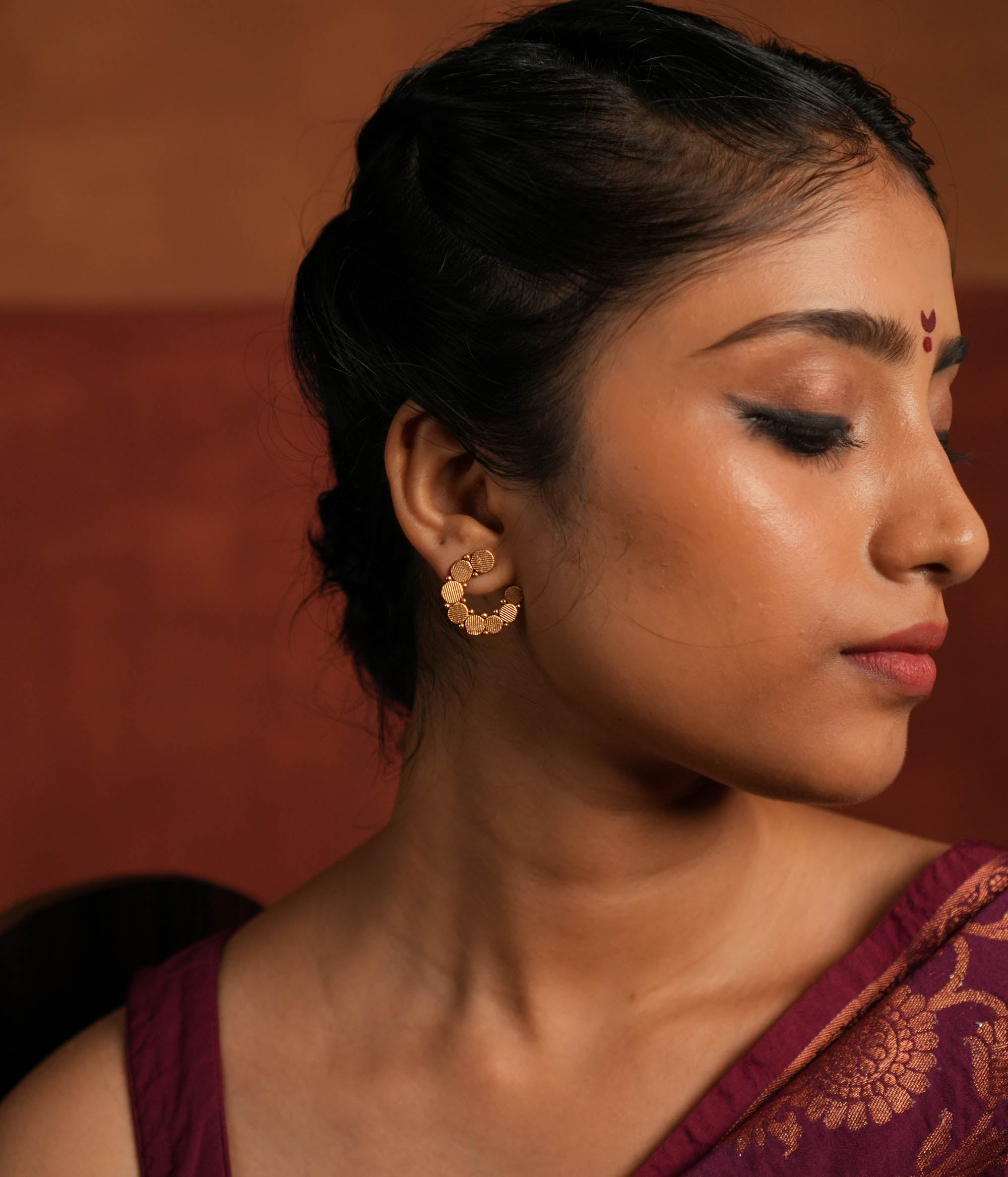 These gold-plated silver stud earrings showcase dainty coin-like motifs arranged in a graceful circular pattern. Inspired by vintage Kolhapuri tribal designs, they blend tradition with elegance, making them a timeless addition to any jewelry collection.
