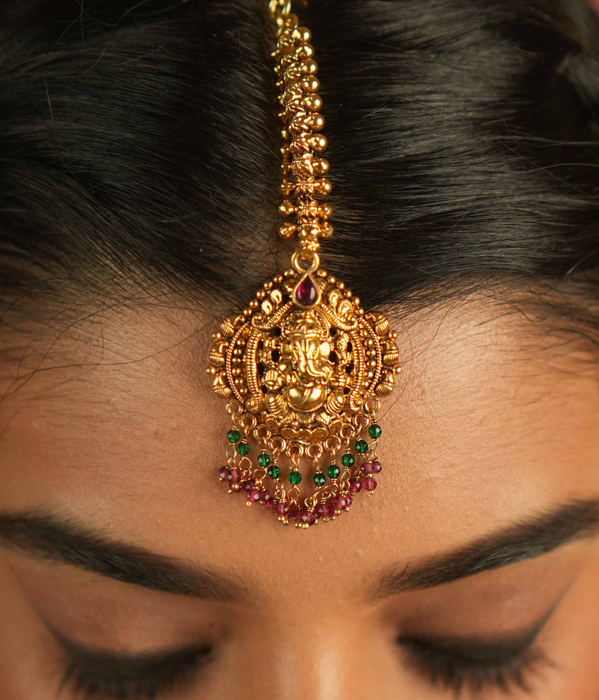 Sacred elegance reimagined! This gold-plated maangtika, adorned with a Lord Ganesha motif, glows with red spinel stones and beads, embodying tradition and spiritual grace.