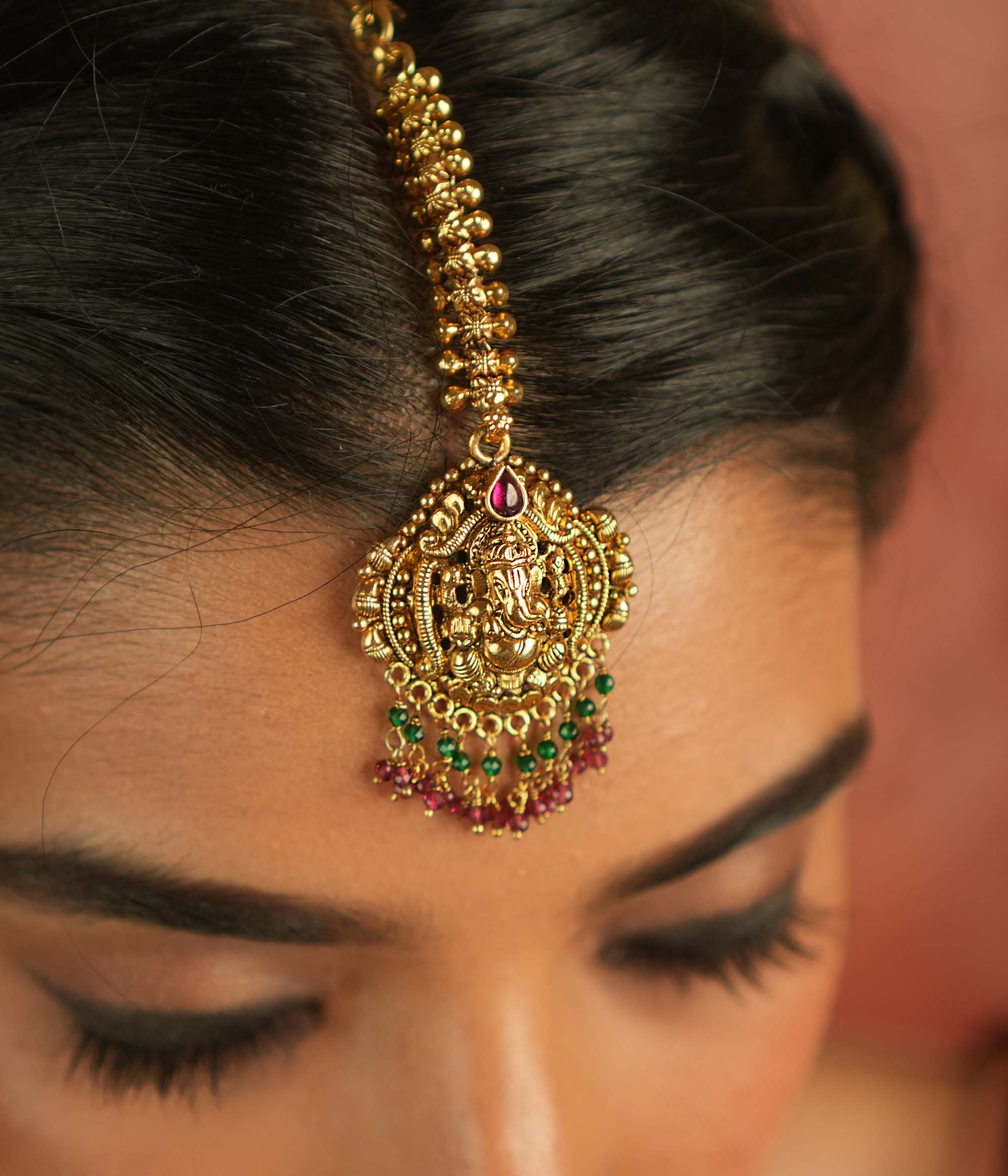 Sacred elegance reimagined! This gold-plated maangtika, adorned with a Lord Ganesha motif, glows with red spinel stones and beads, embodying tradition and spiritual grace.