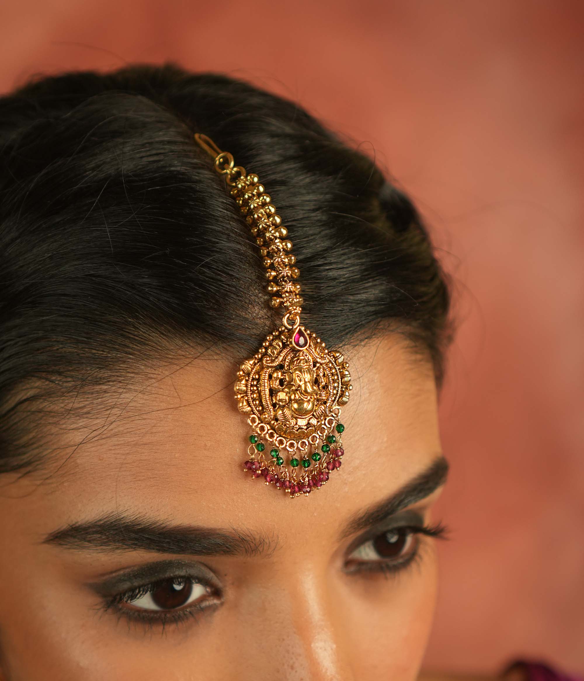 Sacred elegance reimagined! This gold-plated maangtika, adorned with a Lord Ganesha motif, glows with red spinel stones and beads, embodying tradition and spiritual grace.