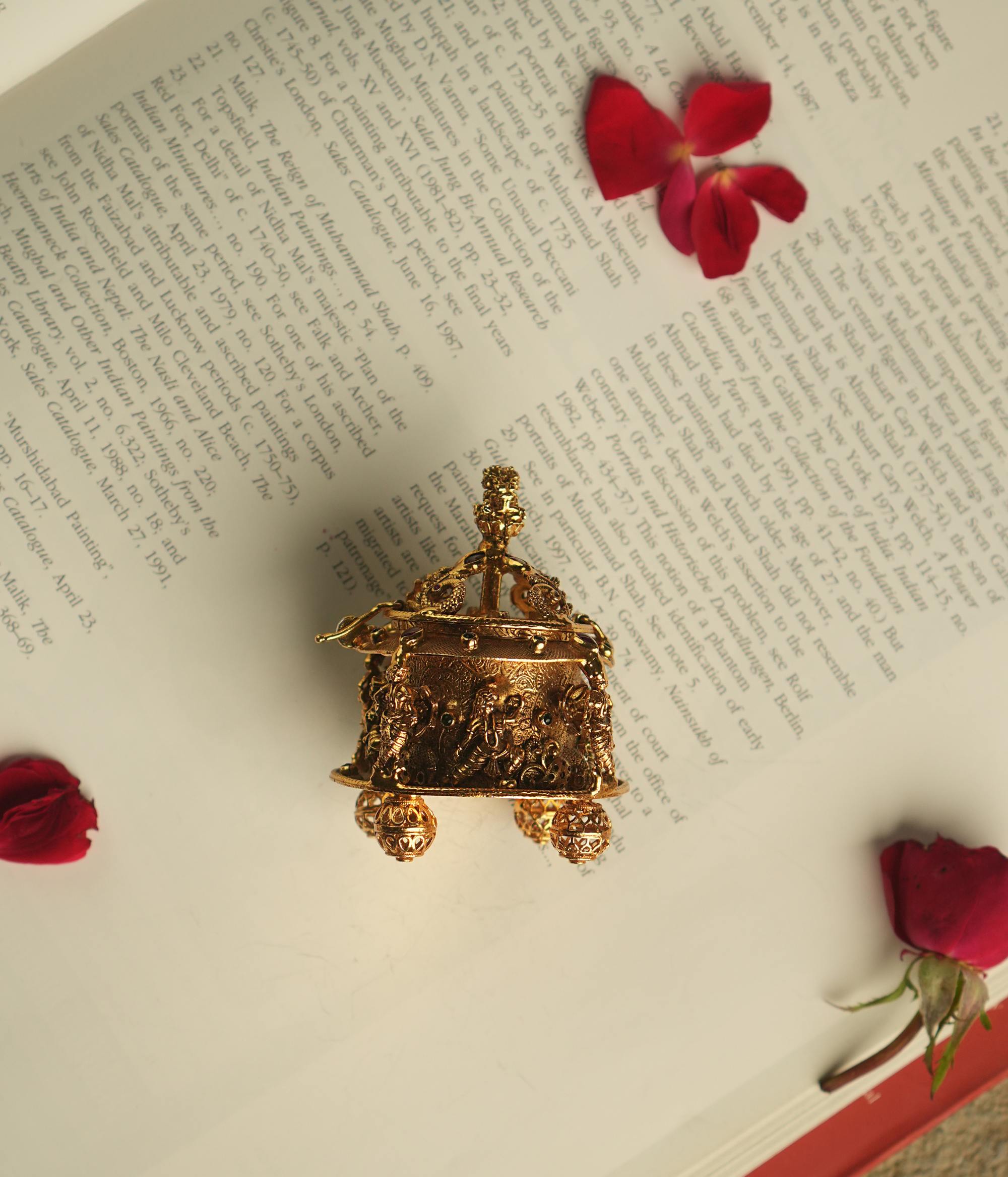 An intricately crafted antique gold-plated silver sindoor case, adorned with temple motifs and red and green kundan stones, embodies the essence of sacred elegance and timeless beauty.