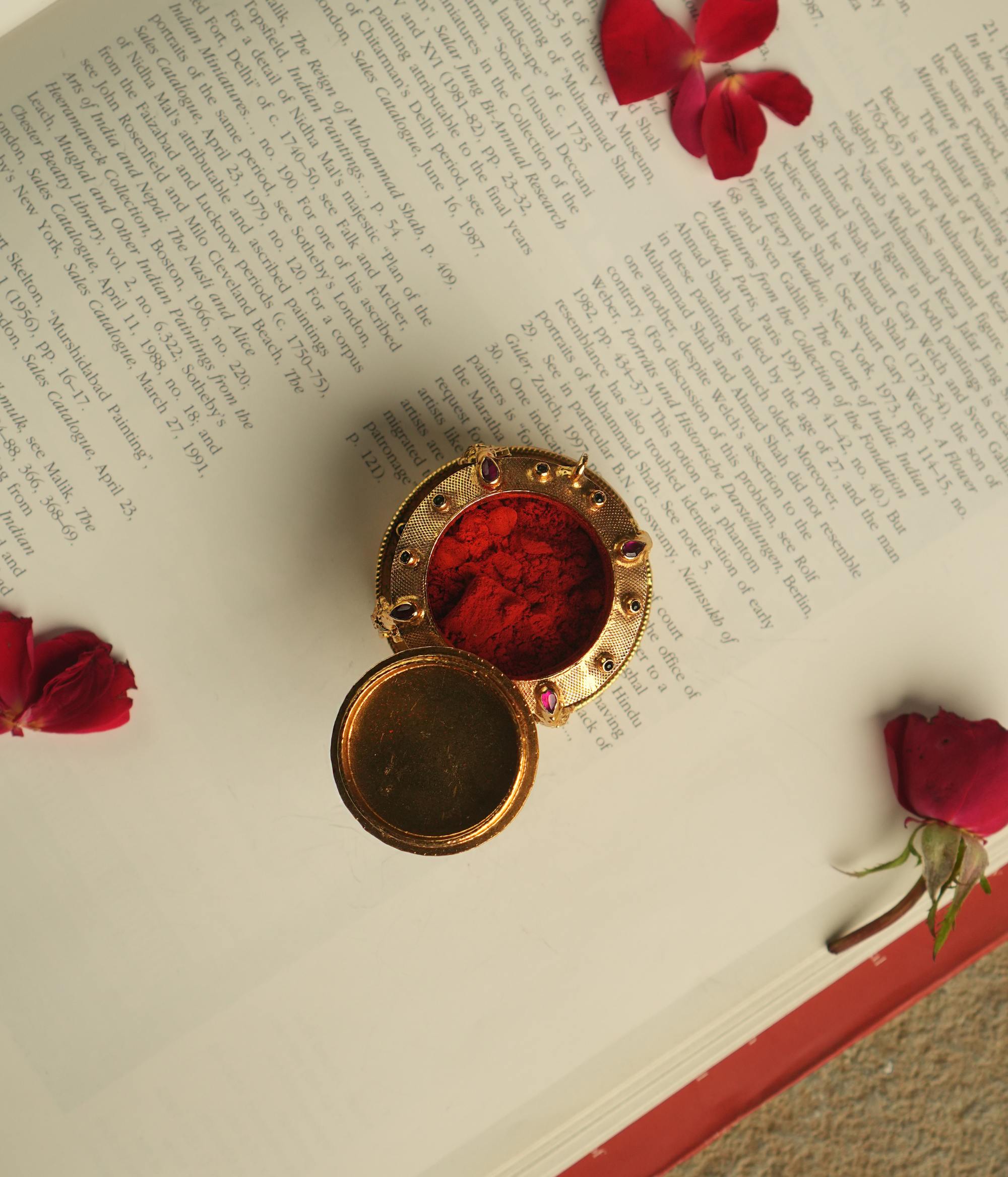 An intricately crafted antique gold-plated silver sindoor case, adorned with temple motifs and red and green kundan stones, embodies the essence of sacred elegance and timeless beauty.