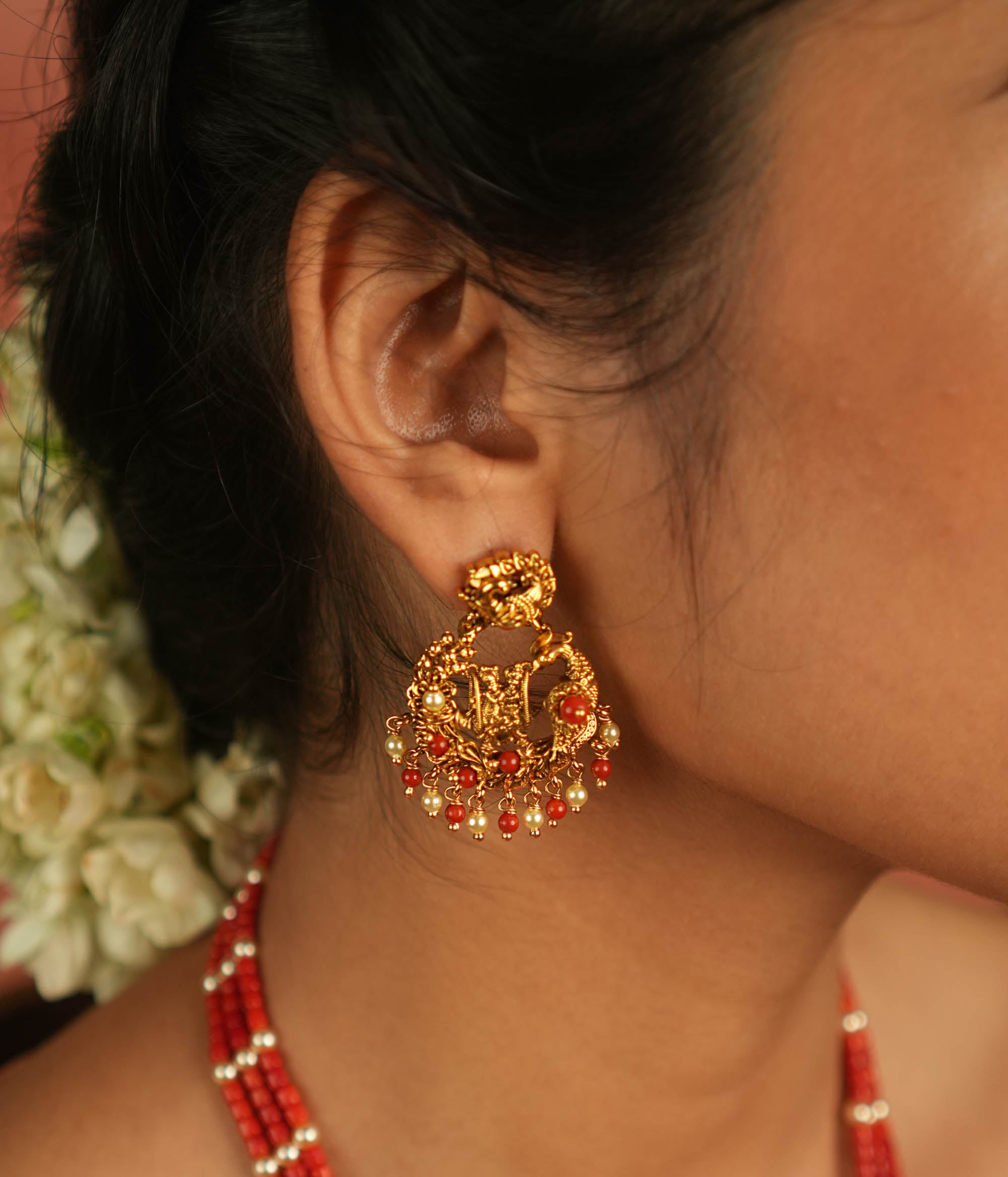 Timeless devotion reimagined! These gold-plated Radha Krishna dangler earrings, framed in an elegant peacock design, shimmer with red beads, embodying divine love and grace.