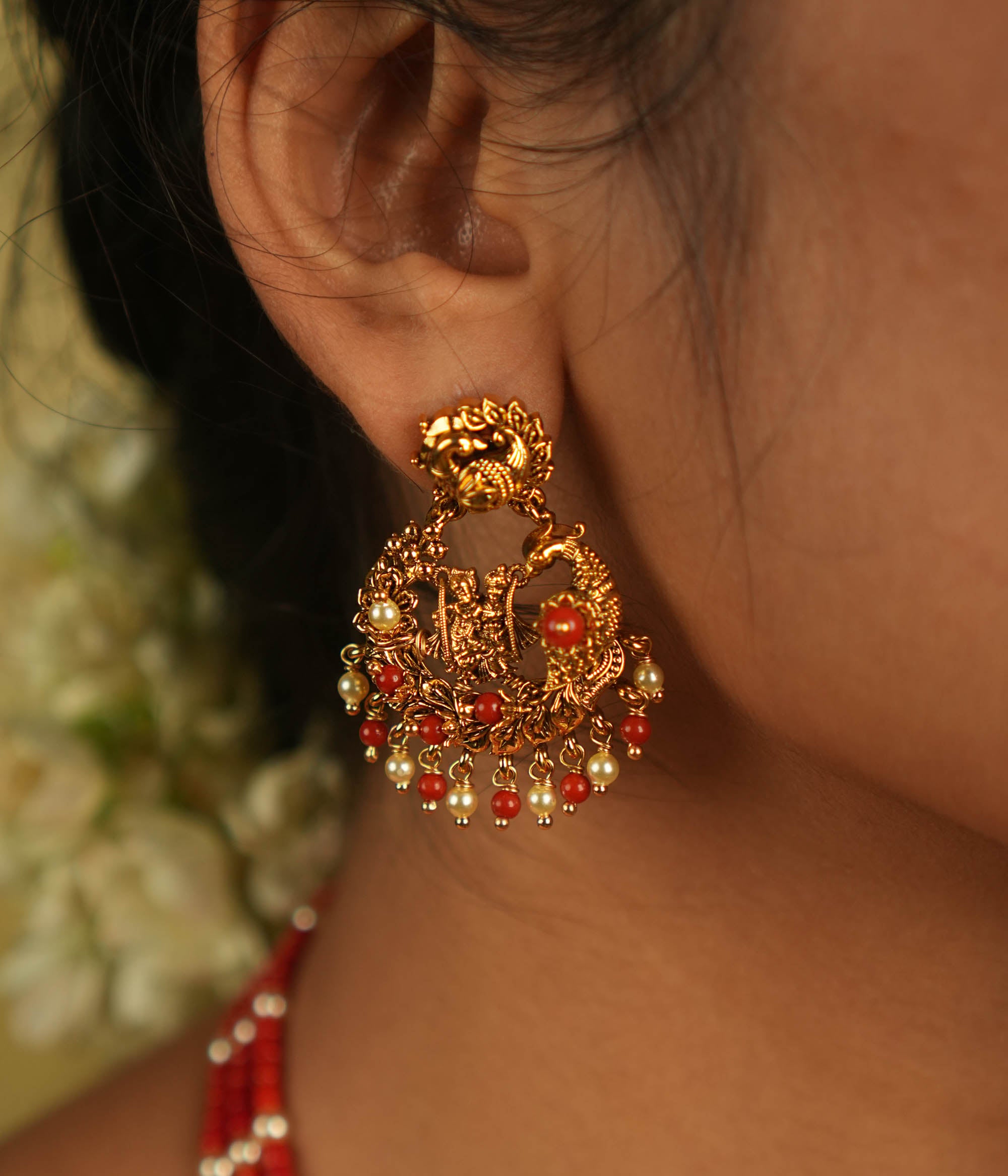 Timeless devotion reimagined! These gold-plated Radha Krishna dangler earrings, framed in an elegant peacock design, shimmer with red beads, embodying divine love and grace.