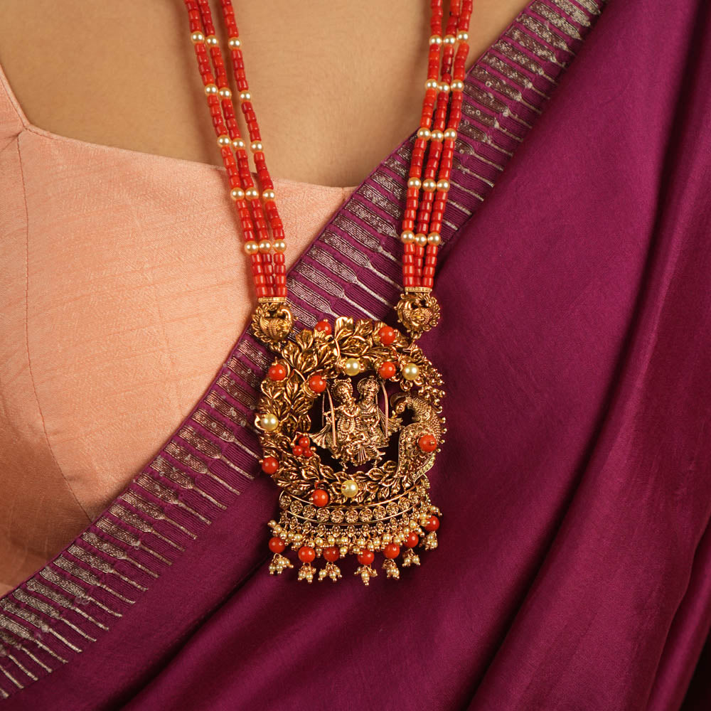 Eternal devotion reimagined! This gold-plated Radha Krishna necklace, set in a peacock-shaped frame, glows with rich red beads, symbolizing timeless love and divine grace.