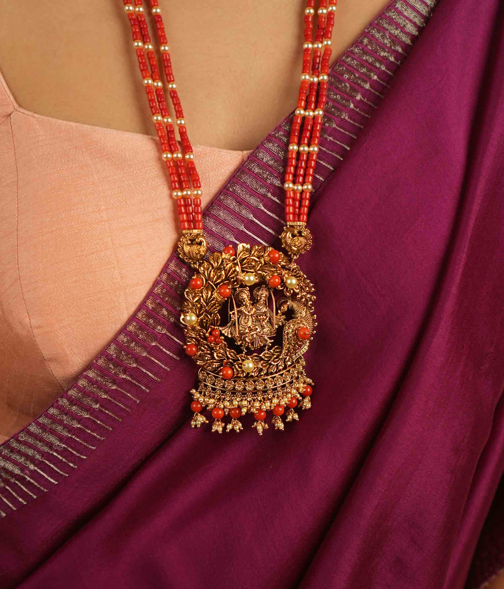 Eternal devotion reimagined! This gold-plated Radha Krishna necklace, set in a peacock-shaped frame, glows with rich red beads, symbolizing timeless love and divine grace.