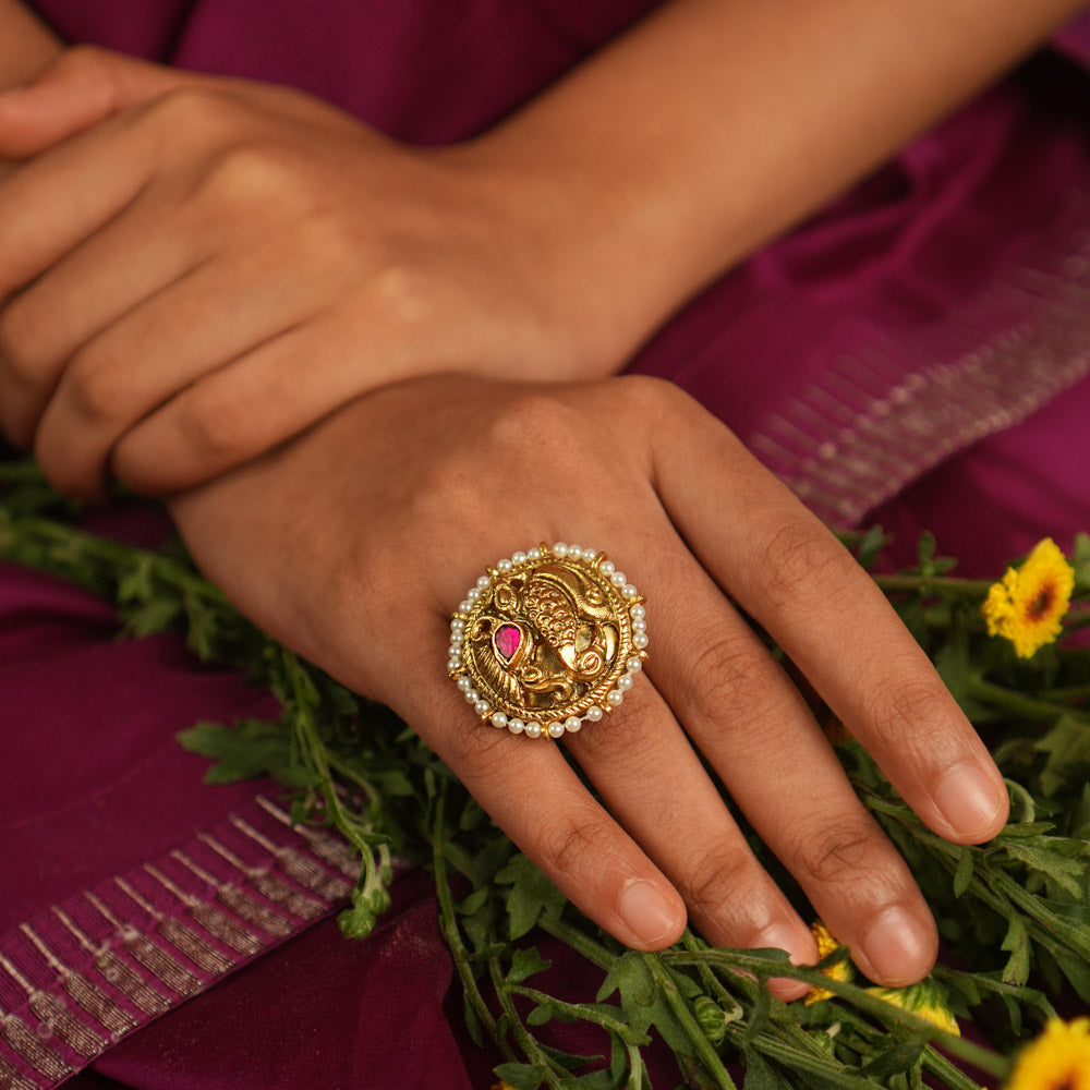 Adorn your finger with this exquisite gold-plated ring, featuring a captivating peacock motif, adorned with radiant red and white Kundan stones. The intricate feathers and Basra pearls add a touch of divine elegance, making this ring a timeless piece of craftsmanship.