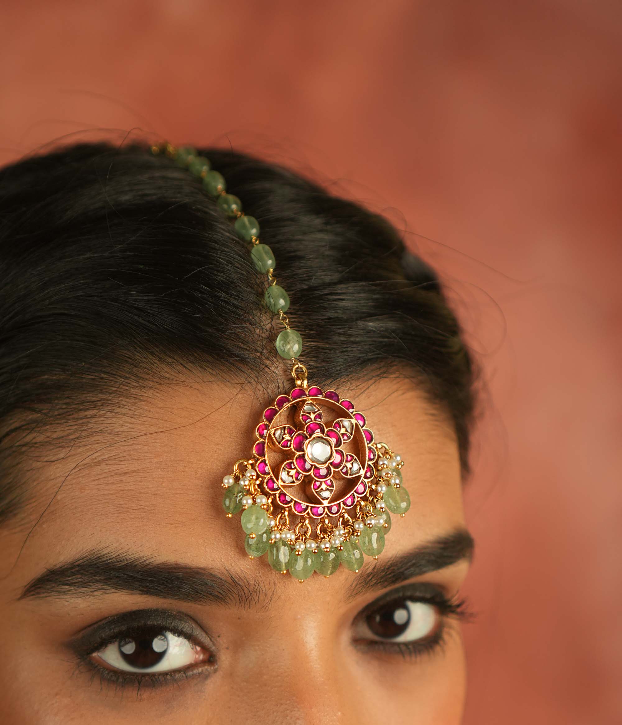 A symbol of blossoming beauty, this maangtika features a stunning combination of red Kundan stones, white Kundan stones, green beads, and pearls. With its romantic allure and vibrant green accents, it is a timeless treasure for the modern bride.