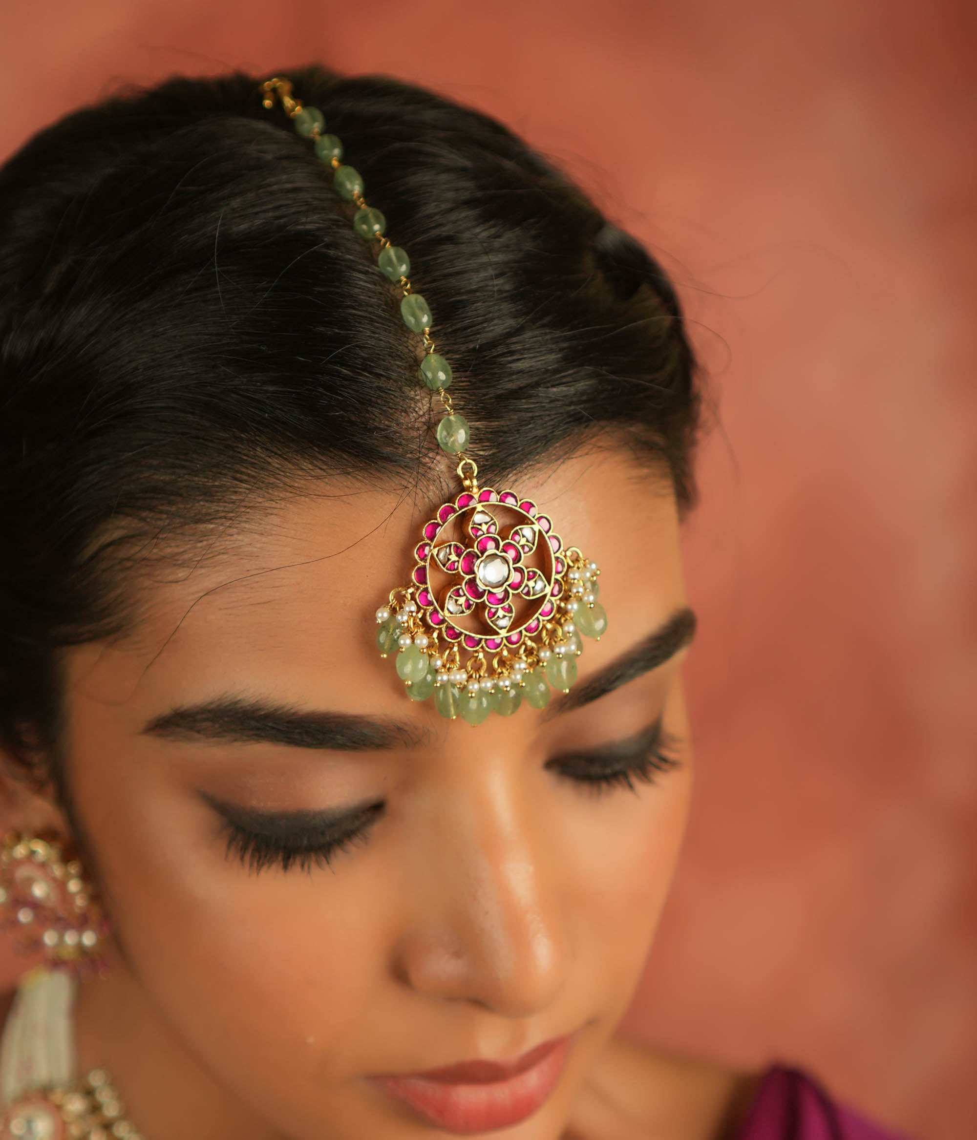 A symbol of blossoming beauty, this maangtika features a stunning combination of red Kundan stones, white Kundan stones, green beads, and pearls. With its romantic allure and vibrant green accents, it is a timeless treasure for the modern bride.