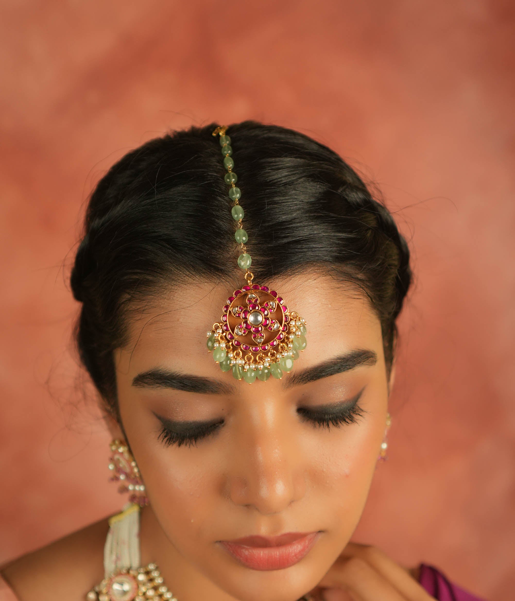 A symbol of blossoming beauty, this maangtika features a stunning combination of red Kundan stones, white Kundan stones, green beads, and pearls. With its romantic allure and vibrant green accents, it is a timeless treasure for the modern bride.
