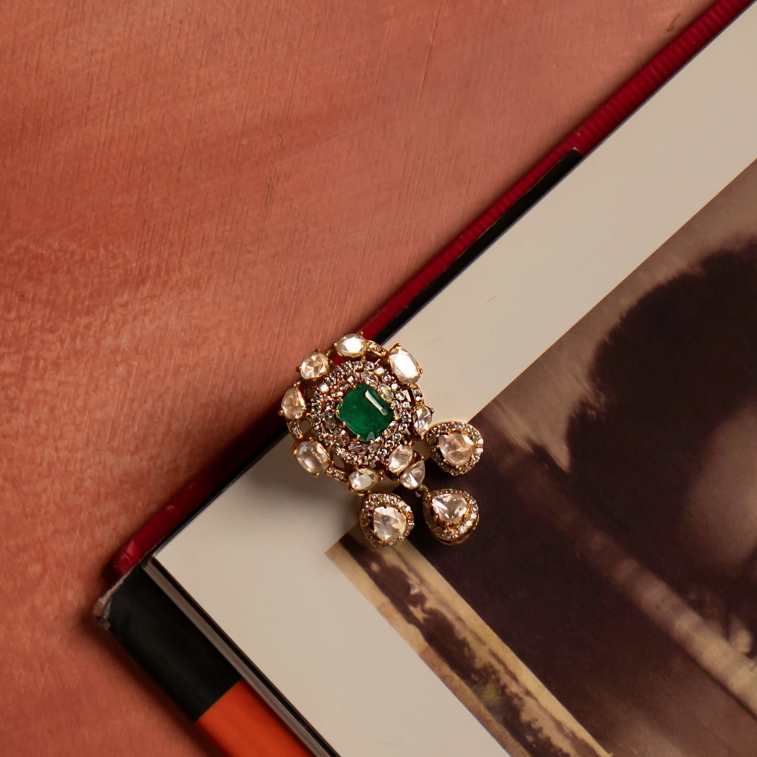 A stunning gold-plated silver pendant featuring a radiant green cut stone at its center, elegantly encircled by shimmering CZ stones and exquisite Polki stones. The design is further enhanced with three delicate Polki stone drops, each beautifully surrounded by CZ stones, adding a touch of sophistication and charm. This intricately crafted pendant exudes timeless elegance, making it a perfect statement piece for any occasion.
