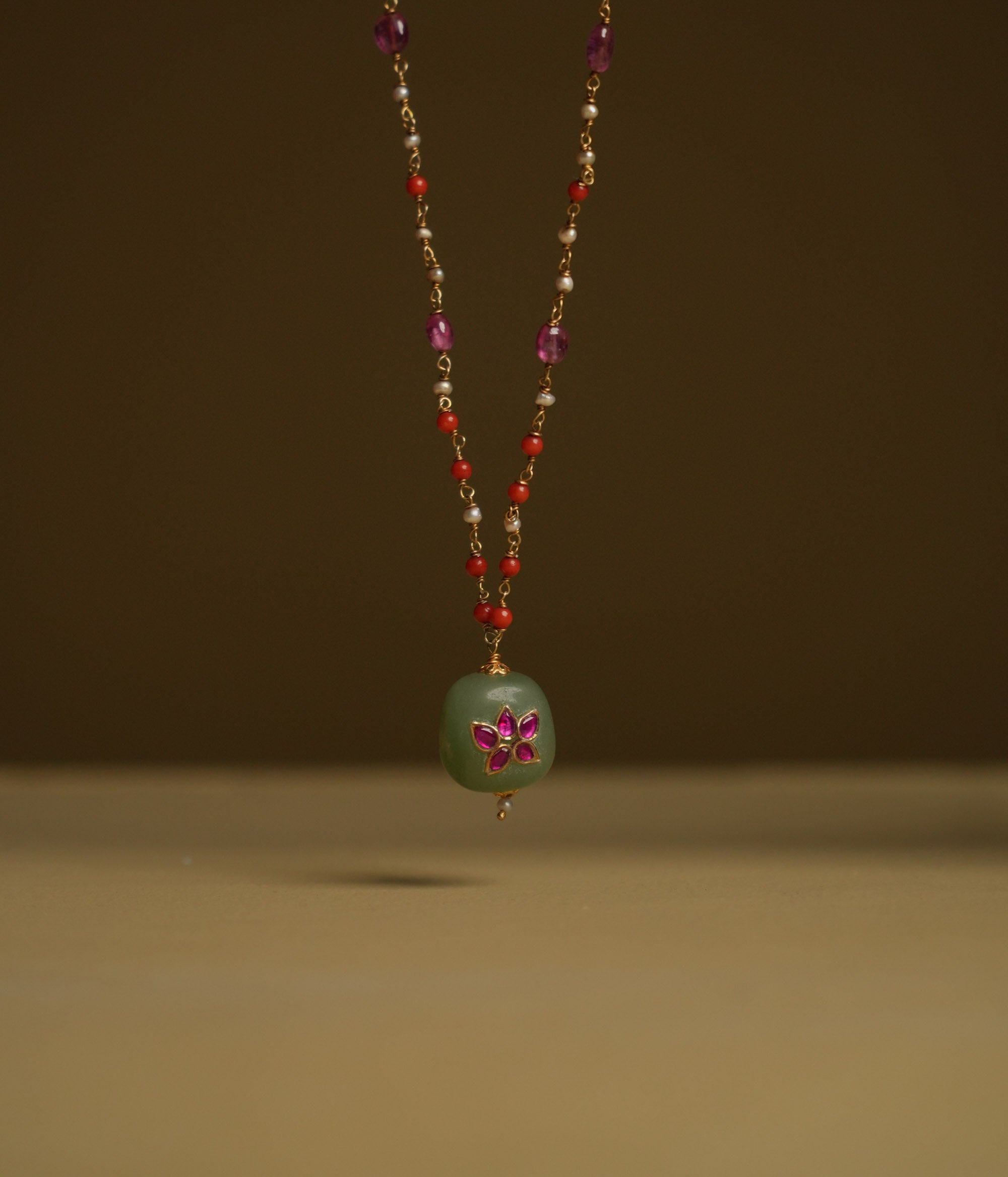A minimal 92.5 sterling silver necklace featuring a natural green stone intricately engraved with pink Kundan meenakari, inspired by Rajput design.