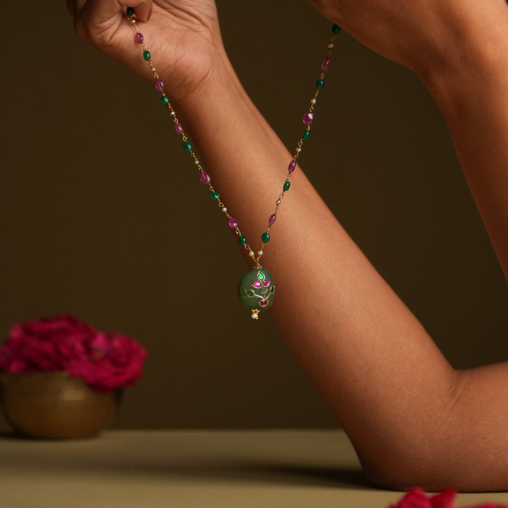 A 92.5 sterling silver necklace featuring a bold green natural stone pendant, adorned with intricate Meenakari Kundan accents in rich purple hues, inspired by vintage Rajput techniques.
