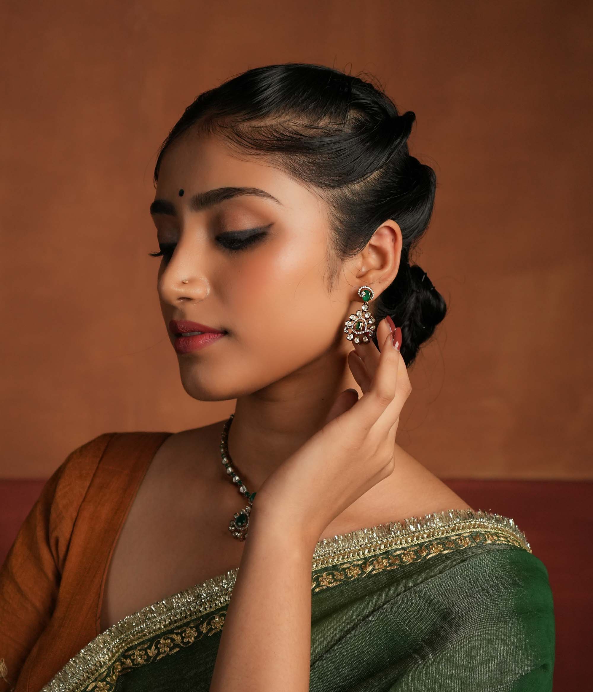 A symphony of Victorian and Oriental charm, these gold-plated silver earrings feature delicate polki and green gemstones. Their floral design, with a lush emerald center encircled by shimmering polki and CZ stones, whispers tales of timeless beauty. Intricate craftsmanship meets regal allure, creating an enchanting statement of elegance.