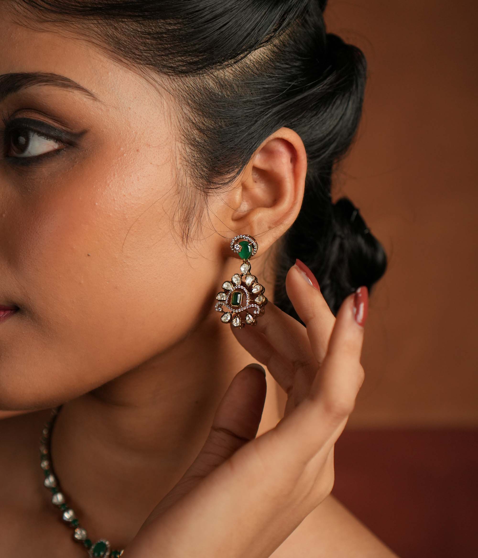 A symphony of Victorian and Oriental charm, these gold-plated silver earrings feature delicate polki and green gemstones. Their floral design, with a lush emerald center encircled by shimmering polki and CZ stones, whispers tales of timeless beauty. Intricate craftsmanship meets regal allure, creating an enchanting statement of elegance.