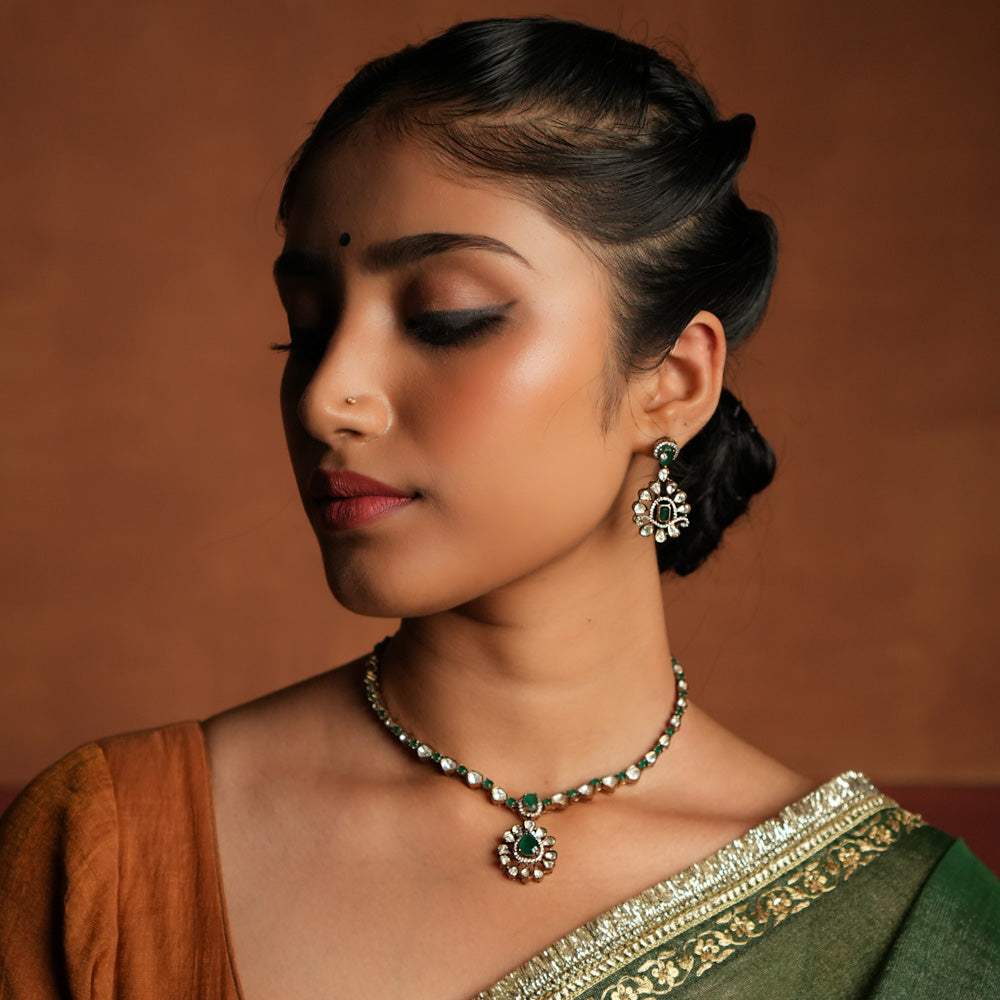 A symphony of Victorian and Oriental charm, this gold-plated silver chain features delicate polki and green gemstones. Its floral pendant, with a lush emerald center encircled by shimmering polki and CZ stones, whispers tales of timeless beauty. Intricate craftsmanship meets regal allure, creating an enchanting statement of elegance.