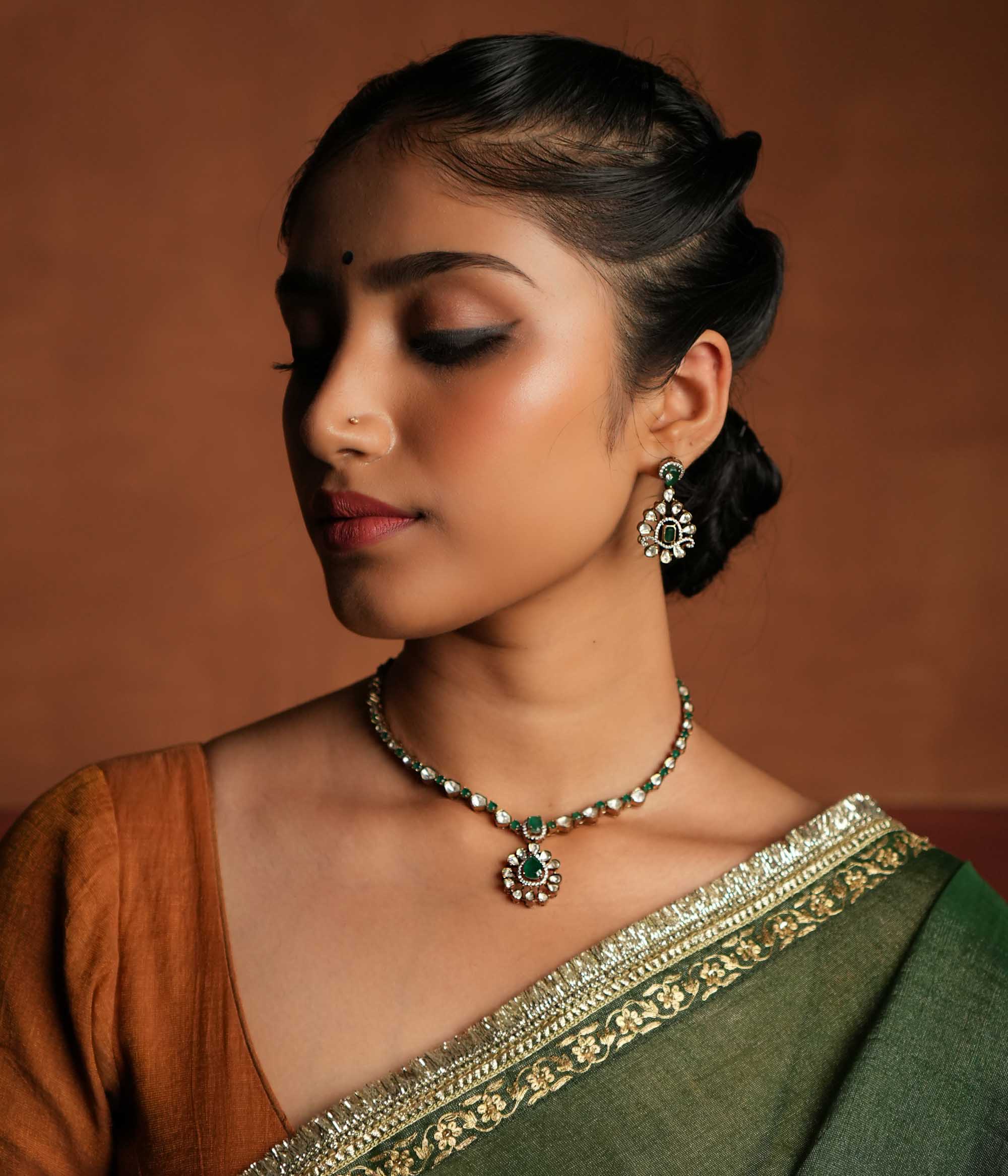 A symphony of Victorian and Oriental charm, this gold-plated silver chain features delicate polki and green gemstones. Its floral pendant, with a lush emerald center encircled by shimmering polki and CZ stones, whispers tales of timeless beauty. Intricate craftsmanship meets regal allure, creating an enchanting statement of elegance.