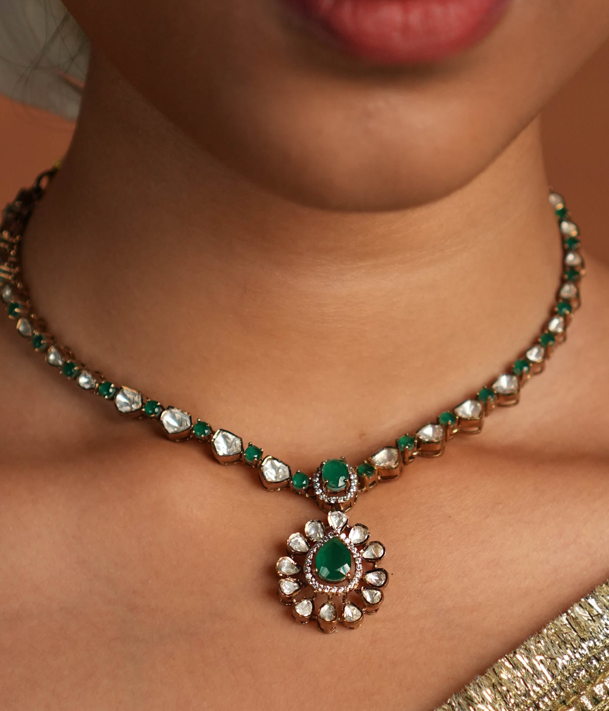 A symphony of Victorian and Oriental charm, this gold-plated silver chain features delicate polki and green gemstones. Its floral pendant, with a lush emerald center encircled by shimmering polki and CZ stones, whispers tales of timeless beauty. Intricate craftsmanship meets regal allure, creating an enchanting statement of elegance.