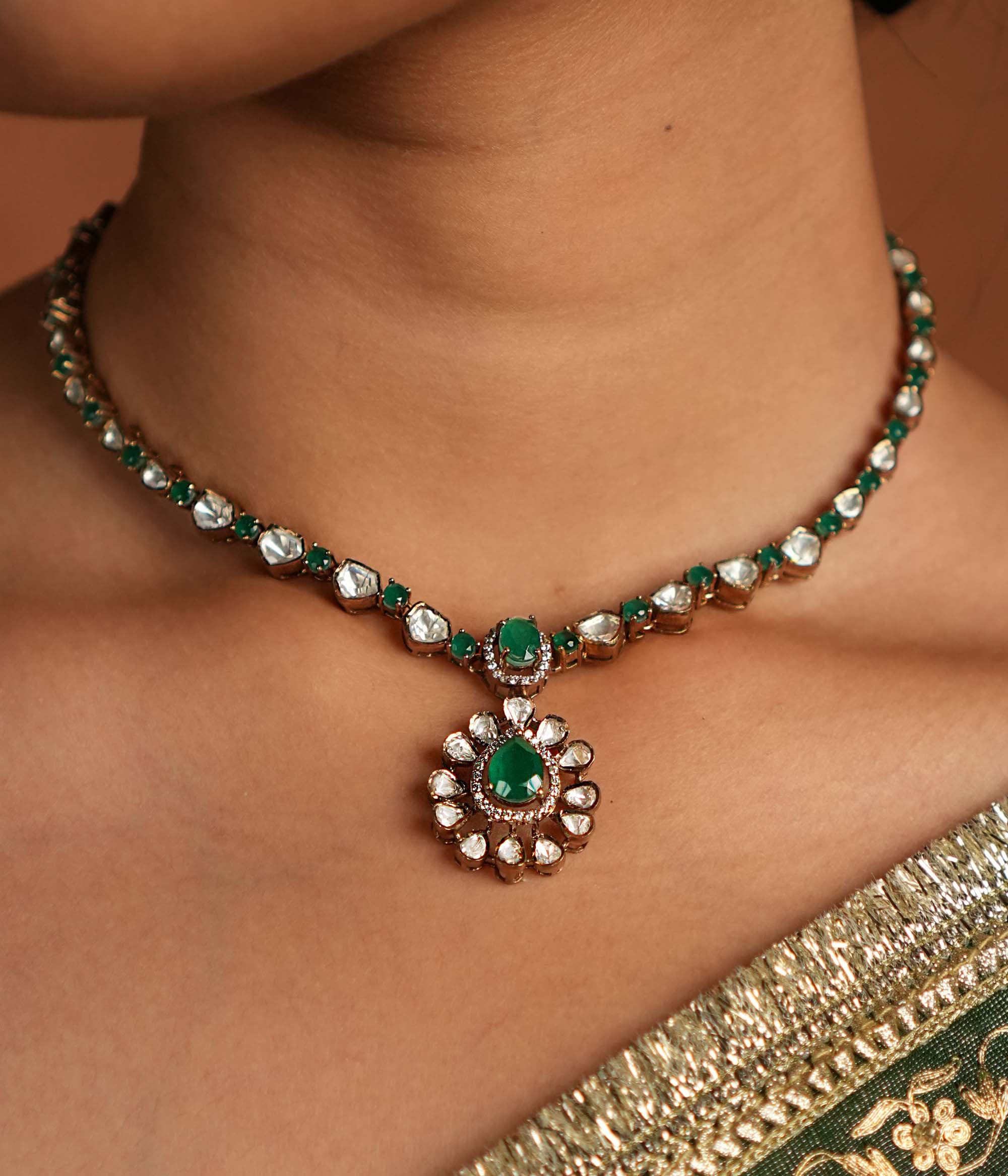 A symphony of Victorian and Oriental charm, this gold-plated silver chain features delicate polki and green gemstones. Its floral pendant, with a lush emerald center encircled by shimmering polki and CZ stones, whispers tales of timeless beauty. Intricate craftsmanship meets regal allure, creating an enchanting statement of elegance.