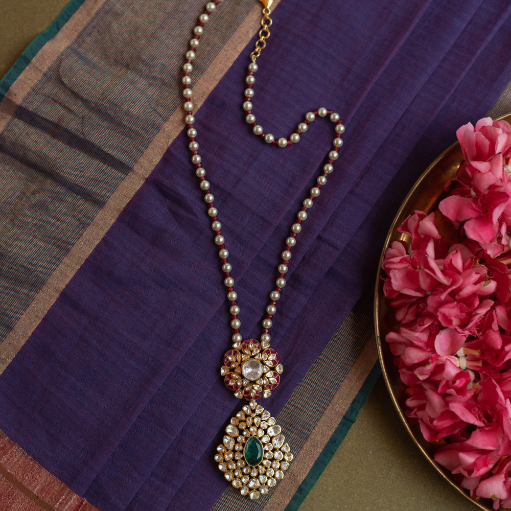 Floral Polki necklace with emerald center, red Kundan accents, and pearl string.