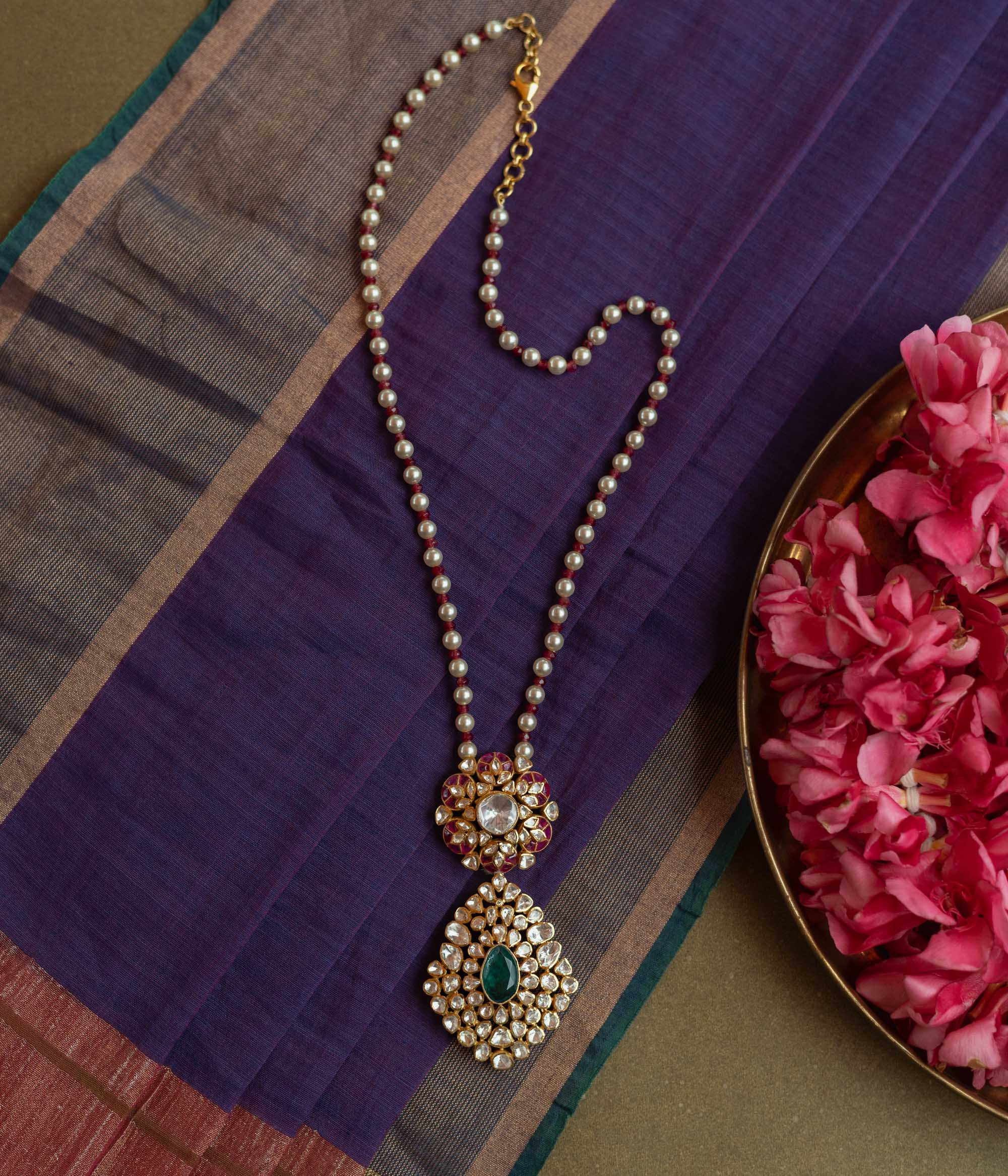 Floral Polki necklace with emerald center, red Kundan accents, and pearl string.