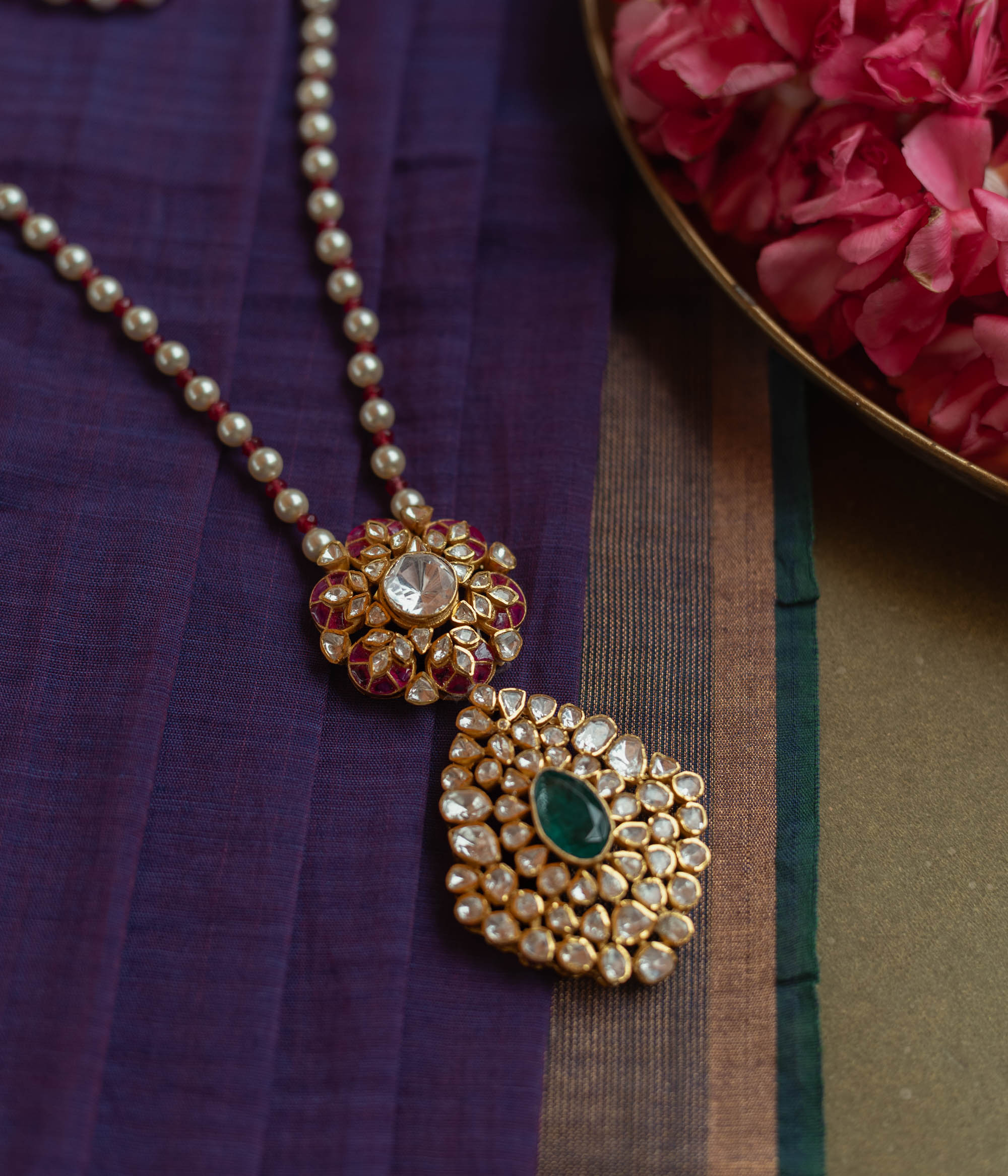 Floral Polki necklace with emerald center, red Kundan accents, and pearl string.