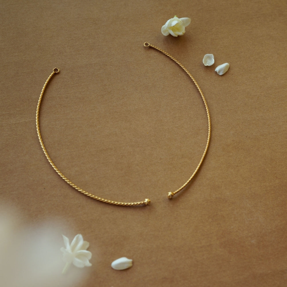 Minimal gold twisted chain from Plain Collection with delicate curve and floral props on brown background.
