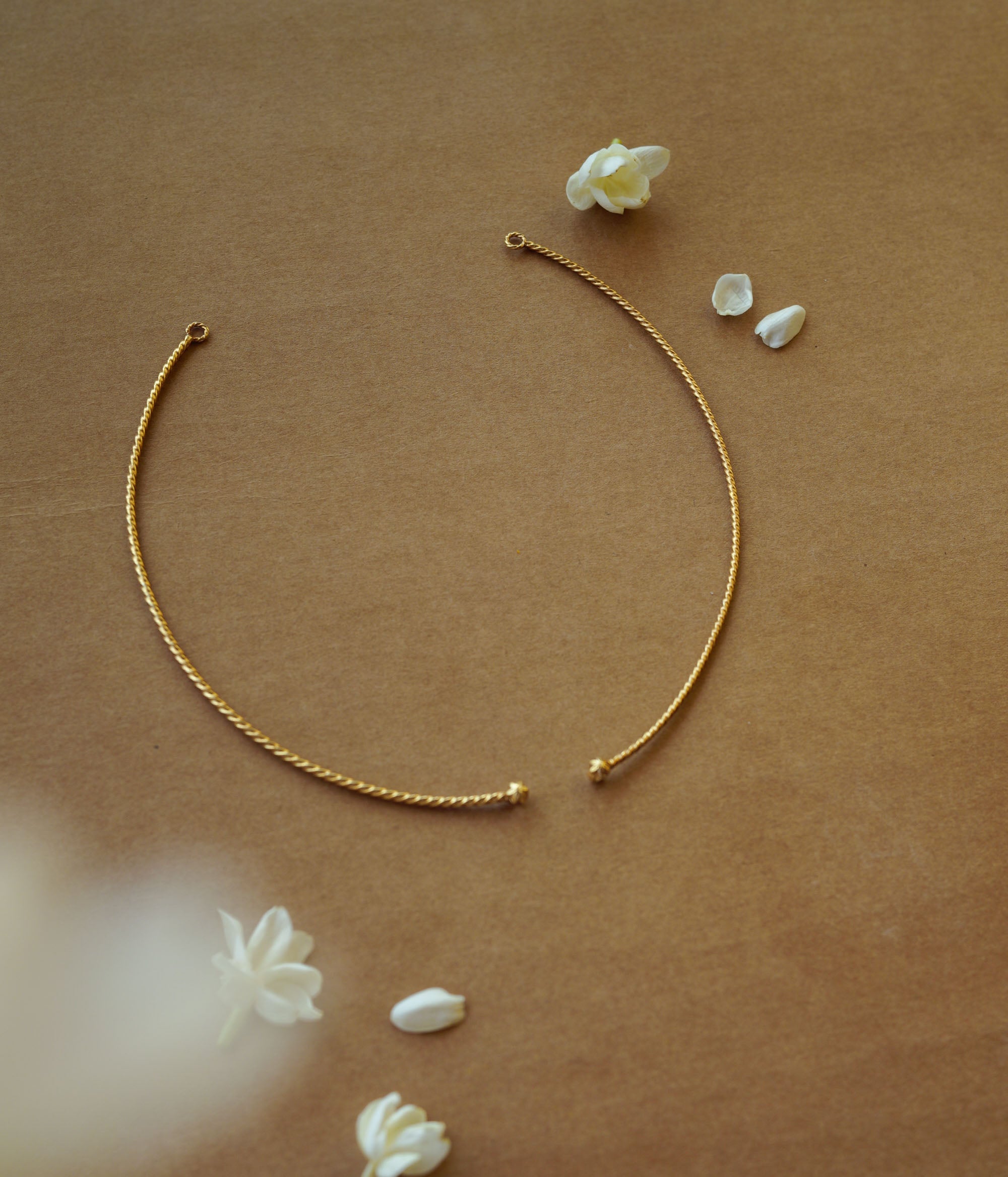 Minimal gold twisted chain from Plain Collection with delicate curve and floral props on brown background.