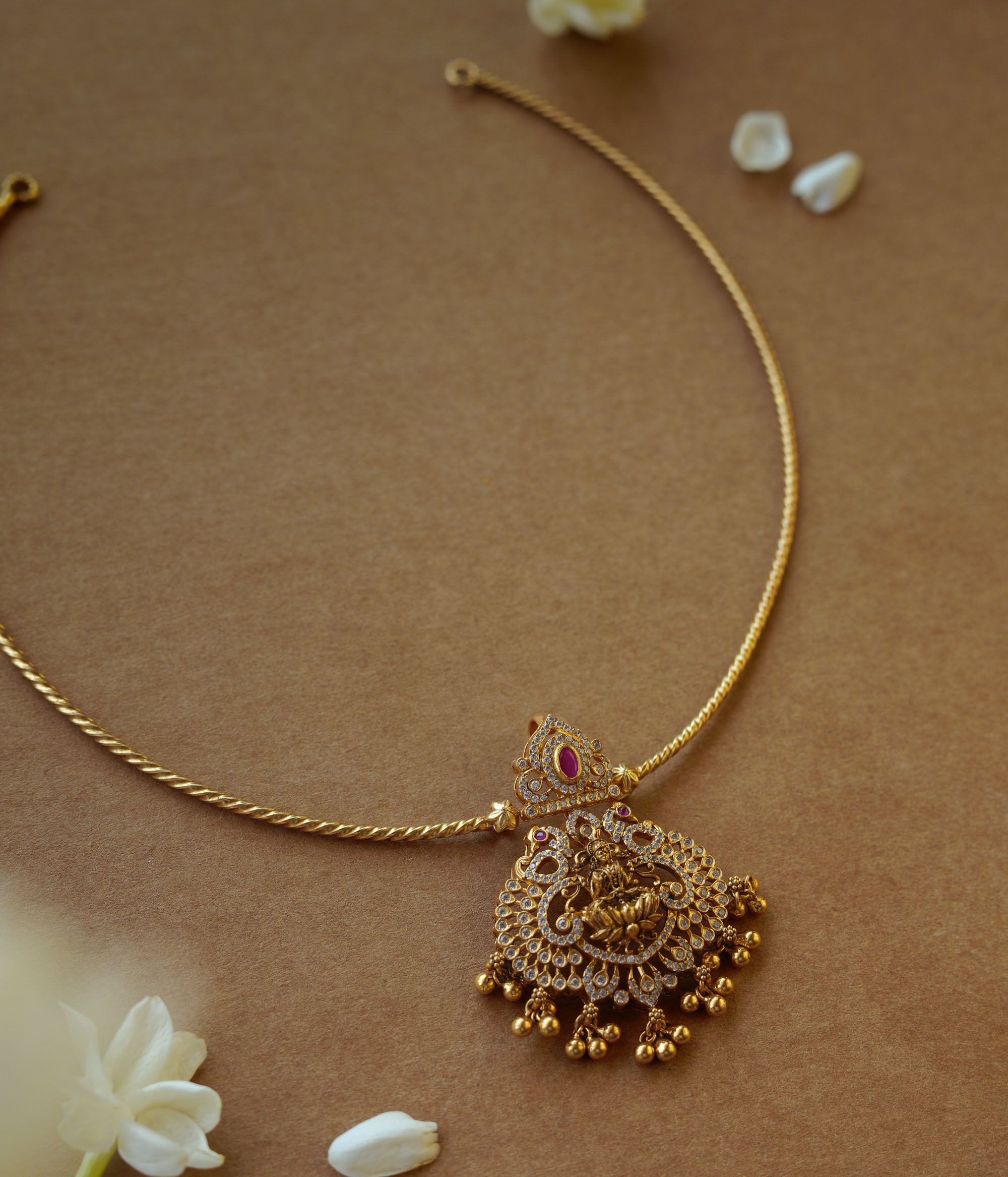 Minimal gold twisted chain from Plain Collection with delicate curve and floral props on brown background.