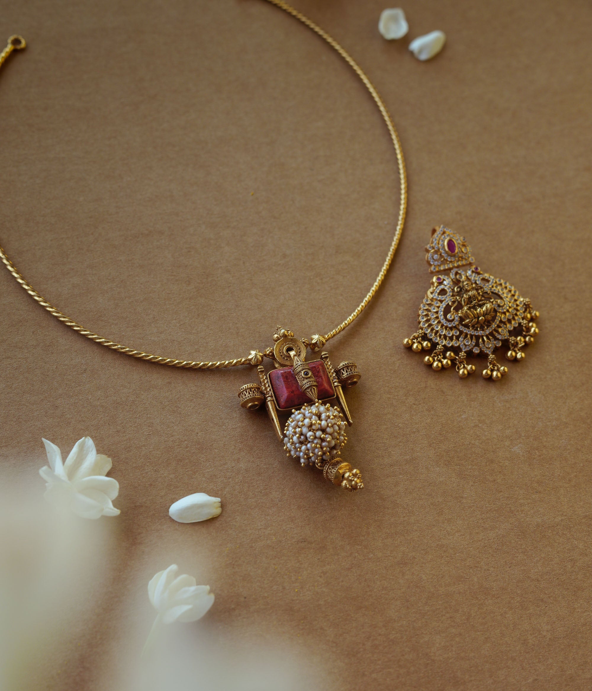 Minimal gold twisted chain from Plain Collection with delicate curve and floral props on brown background.