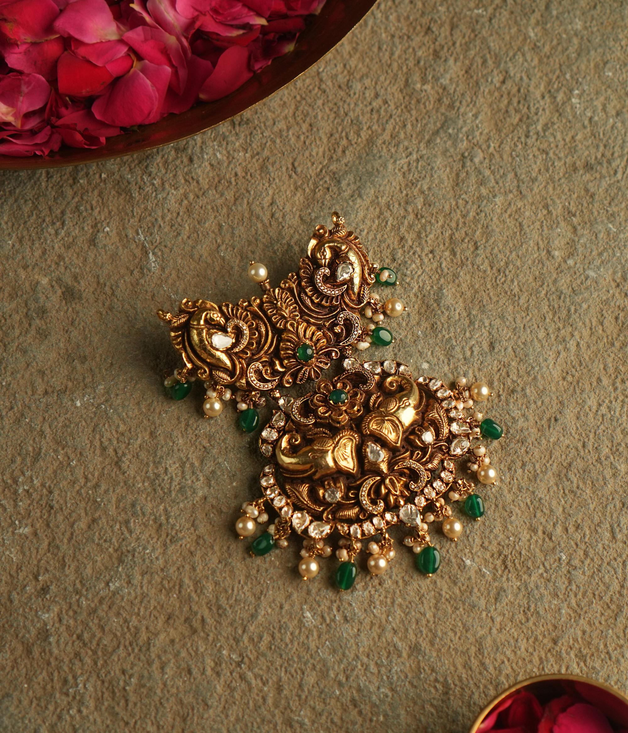 The Nehark Pendant is a mesmerizing fusion of peacock, elephant, and floral motifs, adorned with red, white, and green Kundan stones and golden beads. A timeless masterpiece, it embodies the elegance of ancient traditions, radiating a captivating, mystical glow.