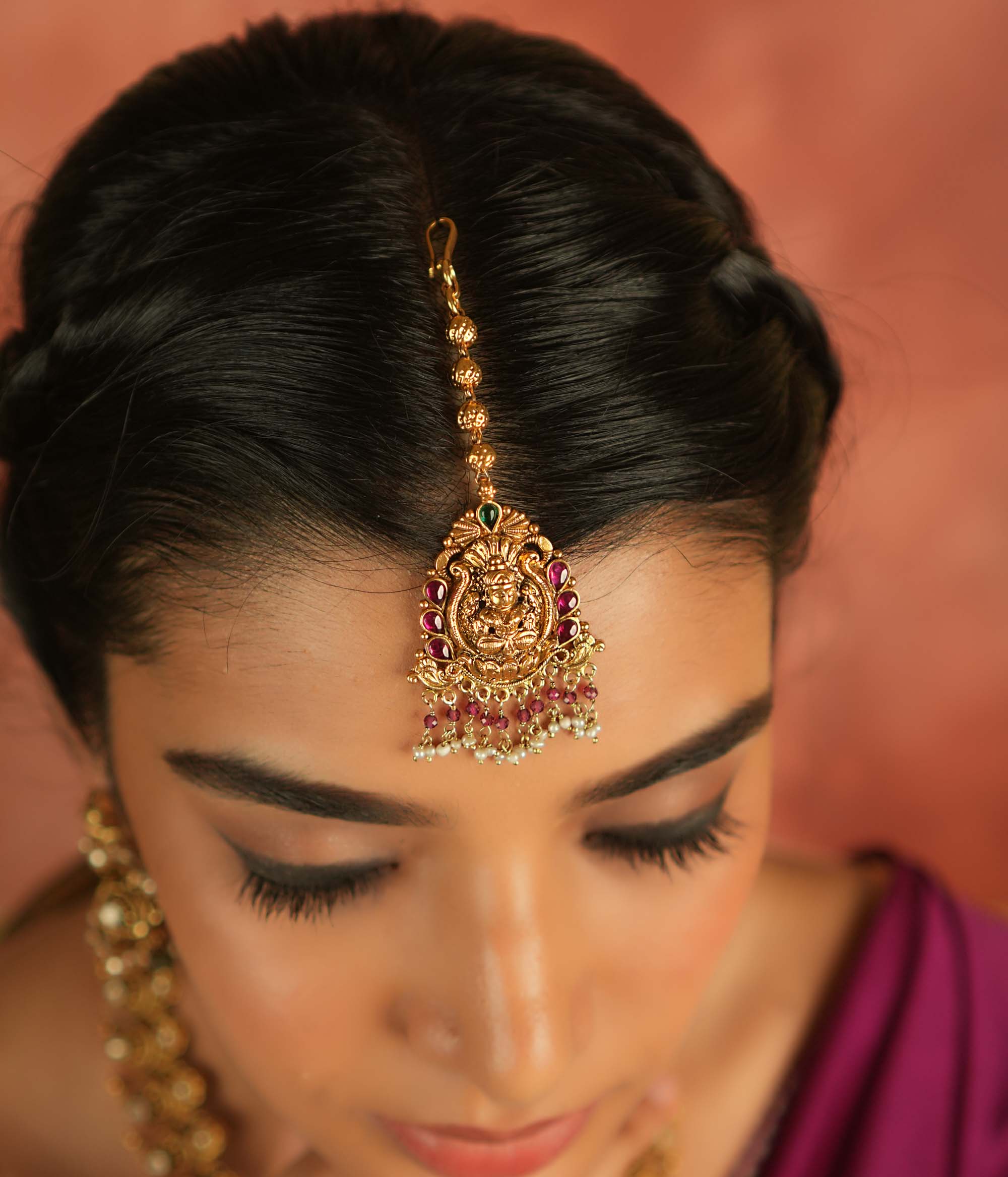 Sacred grace reborn! This gold-plated Lakshmi maangtika, adorned with red and green Kundan stones, glows with white and pink bead droplets—radiating divine blessings and timeless elegance.