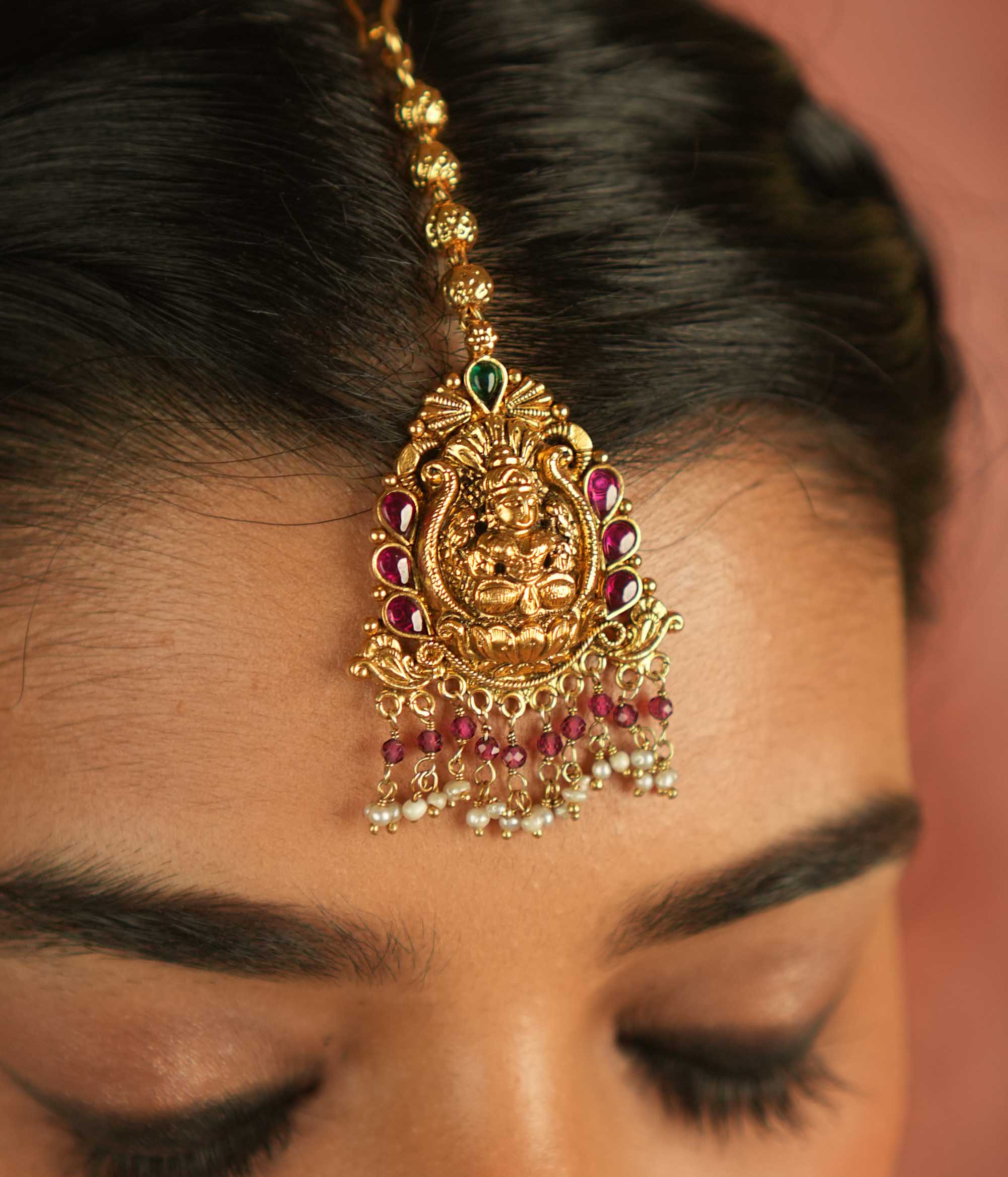 Sacred grace reborn! This gold-plated Lakshmi maangtika, adorned with red and green Kundan stones, glows with white and pink bead droplets—radiating divine blessings and timeless elegance.