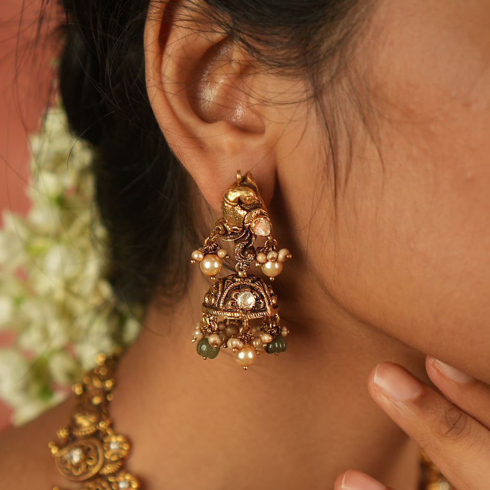 Timeless splendor! These antique gold-plated jhumkas, adorned with a majestic peacock motif, glisten with Polki stones, white pearls, and green beads—echoing regal heritage with every sway.
