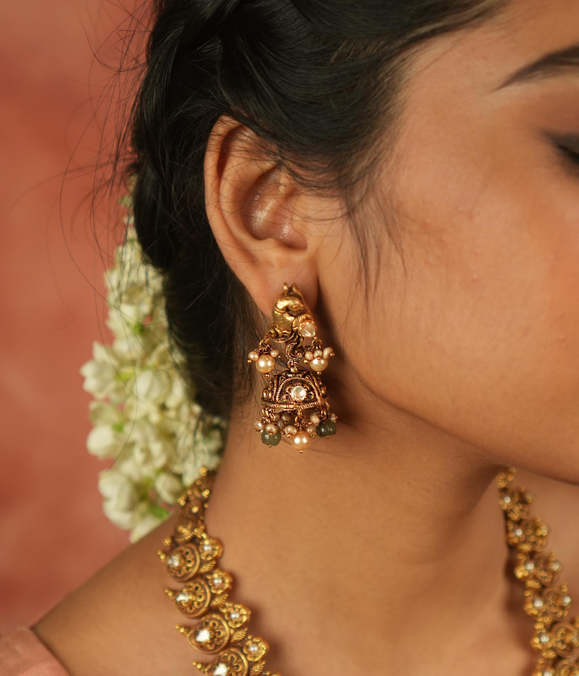 Timeless splendor! These antique gold-plated jhumkas, adorned with a majestic peacock motif, glisten with Polki stones, white pearls, and green beads—echoing regal heritage with every sway.