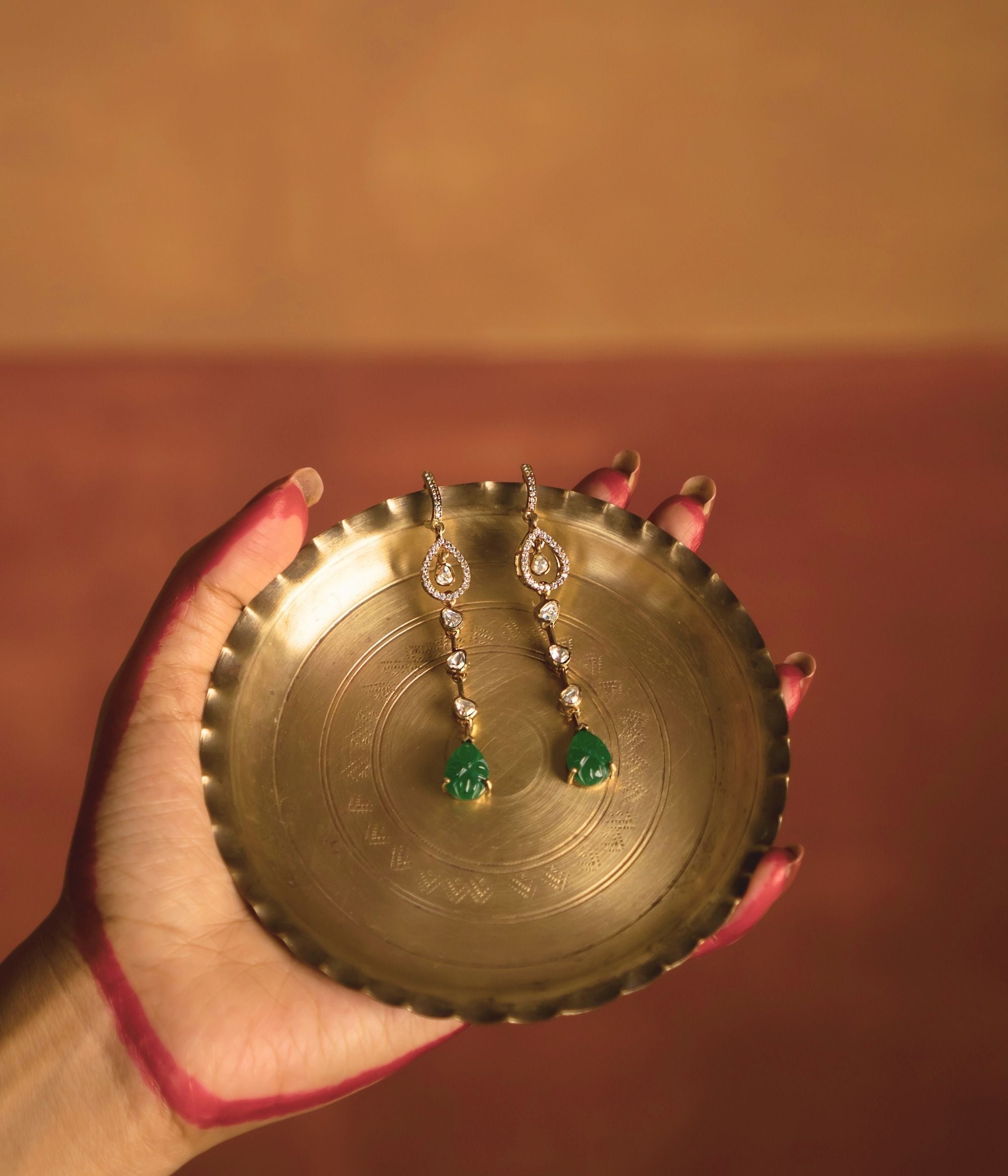 Elegant gold-plated silver push-type drop earrings featuring a dazzling Polki stone at the center, gracefully surrounded by shimmering CZ stones. The design is further enhanced with a vibrant green gemstone, adding a touch of sophistication and timeless charm. Perfect for elevating any traditional or modern ensemble.