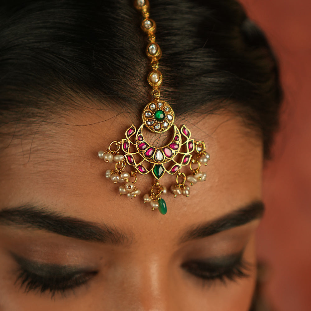 Ethereal elegance! This floral maangtika, adorned with Polki stones and red, green, and white Kundan gems, shimmers with pearls and green beads—whispering celestial charm and timeless grace.